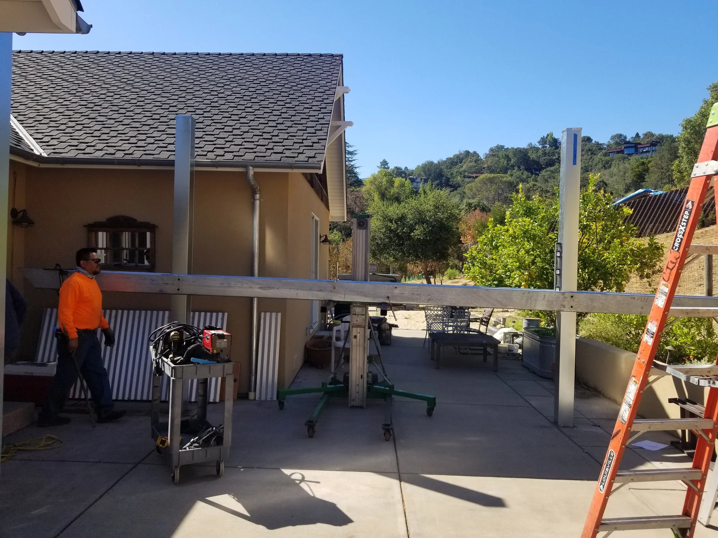 In front of the house with yellow walls there is an iron gray column for an installation in the house's garden. 