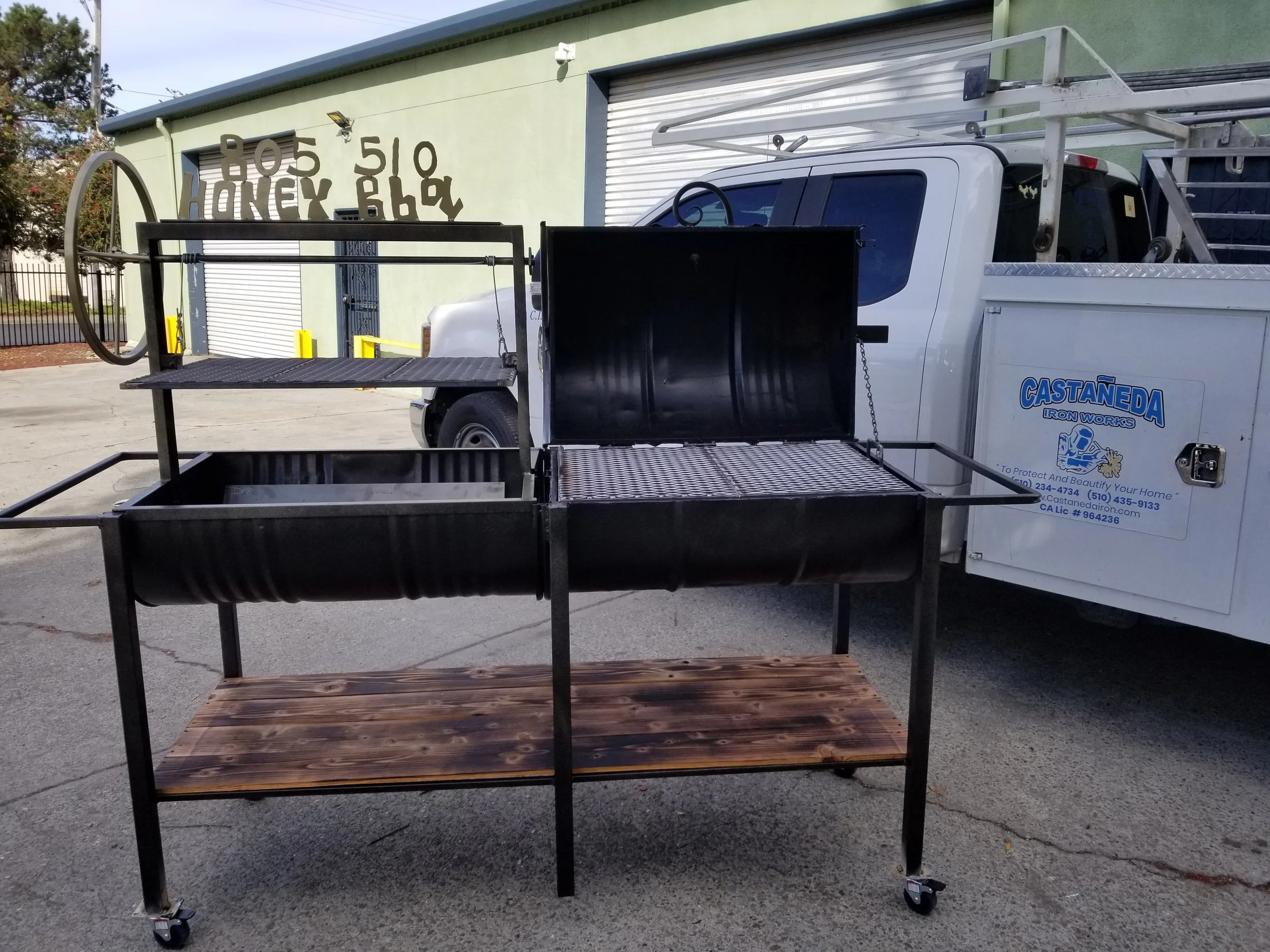 The ultimate in outdoor cooking with our black BBQ pit , expertly crafted in iron, with an elegant wooden base, showing the grills and lids open for better comfort. 