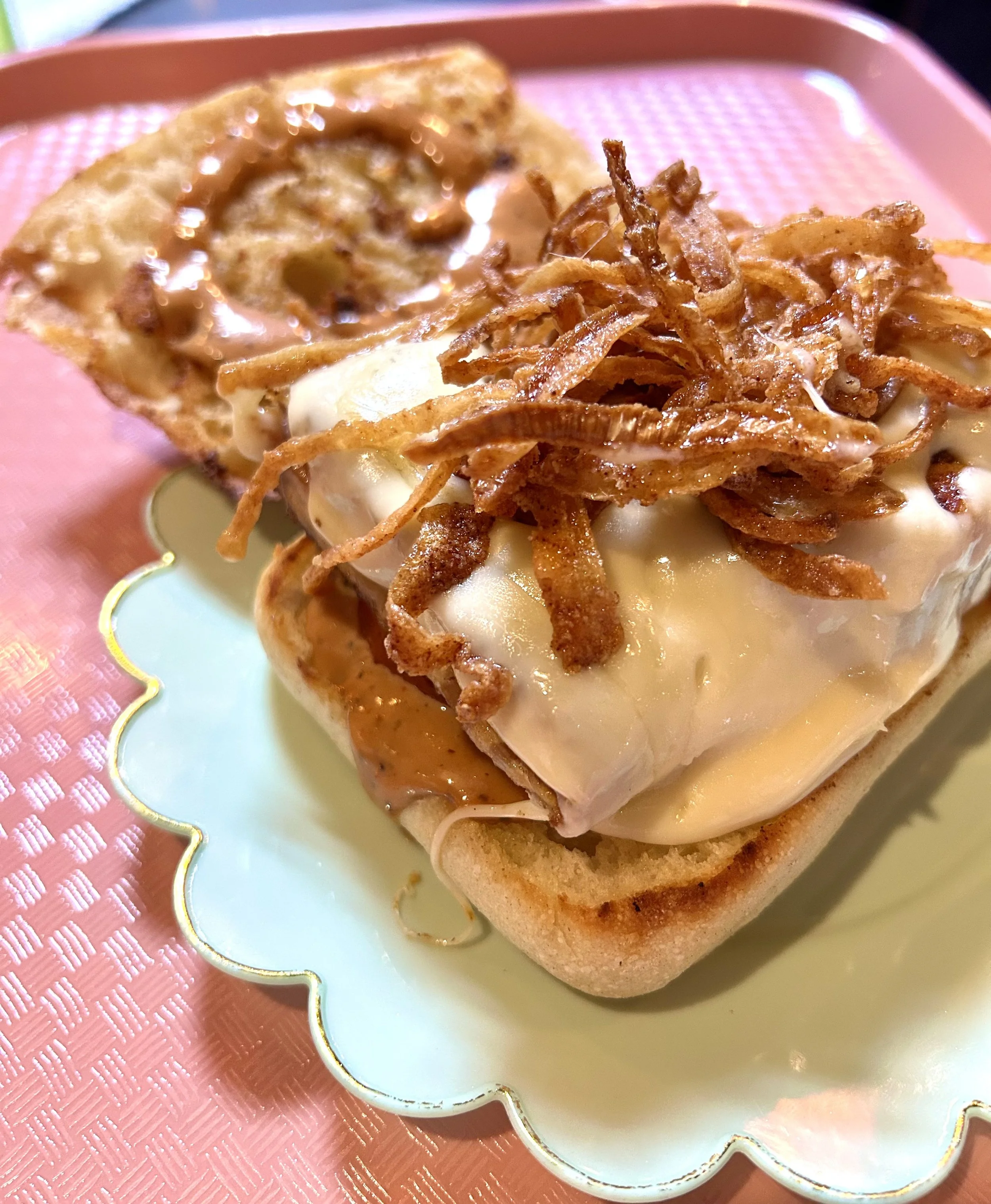 Close-up of an open-faced sandwich with melted cheese, caramelized onions, and a slice of toasted bread on a pastel-colored plate with a pink textured tray underneath.