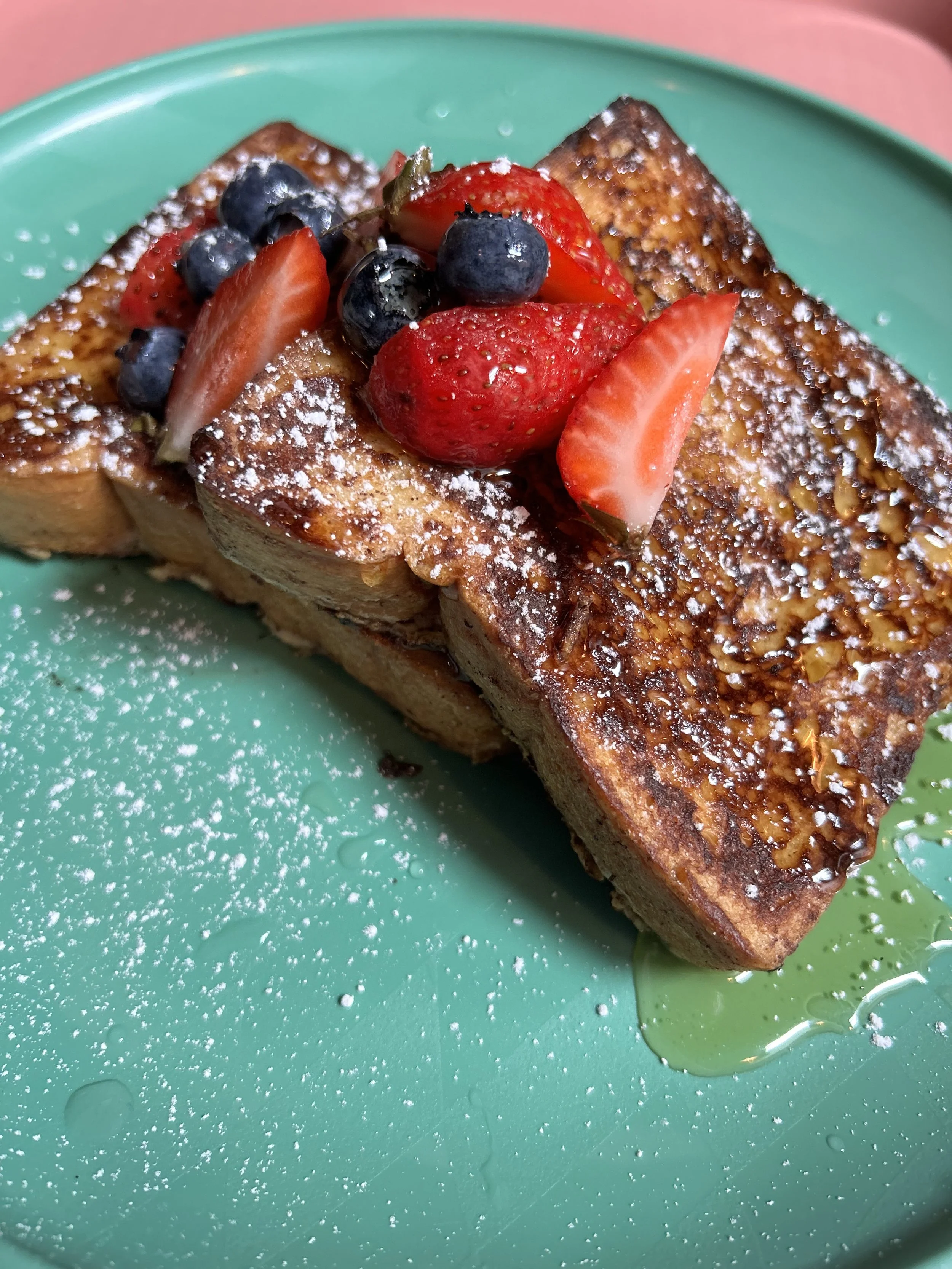French toast topped with strawberries, blueberries, and powdered sugar, served on a green plate.