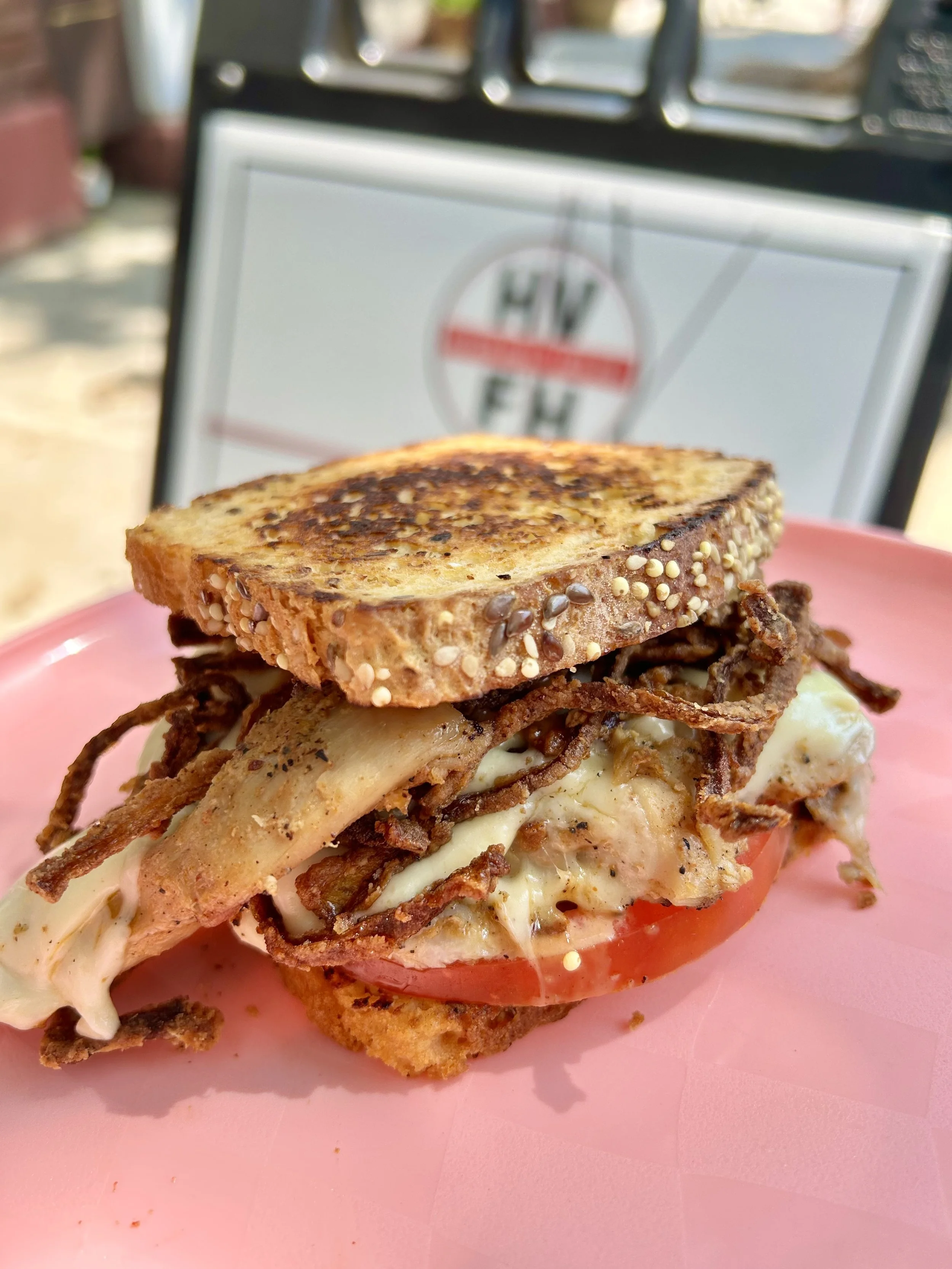 Bacon, egg, tomato, cheese, and multigrain toast sandwich on pink plate with a blurred background.