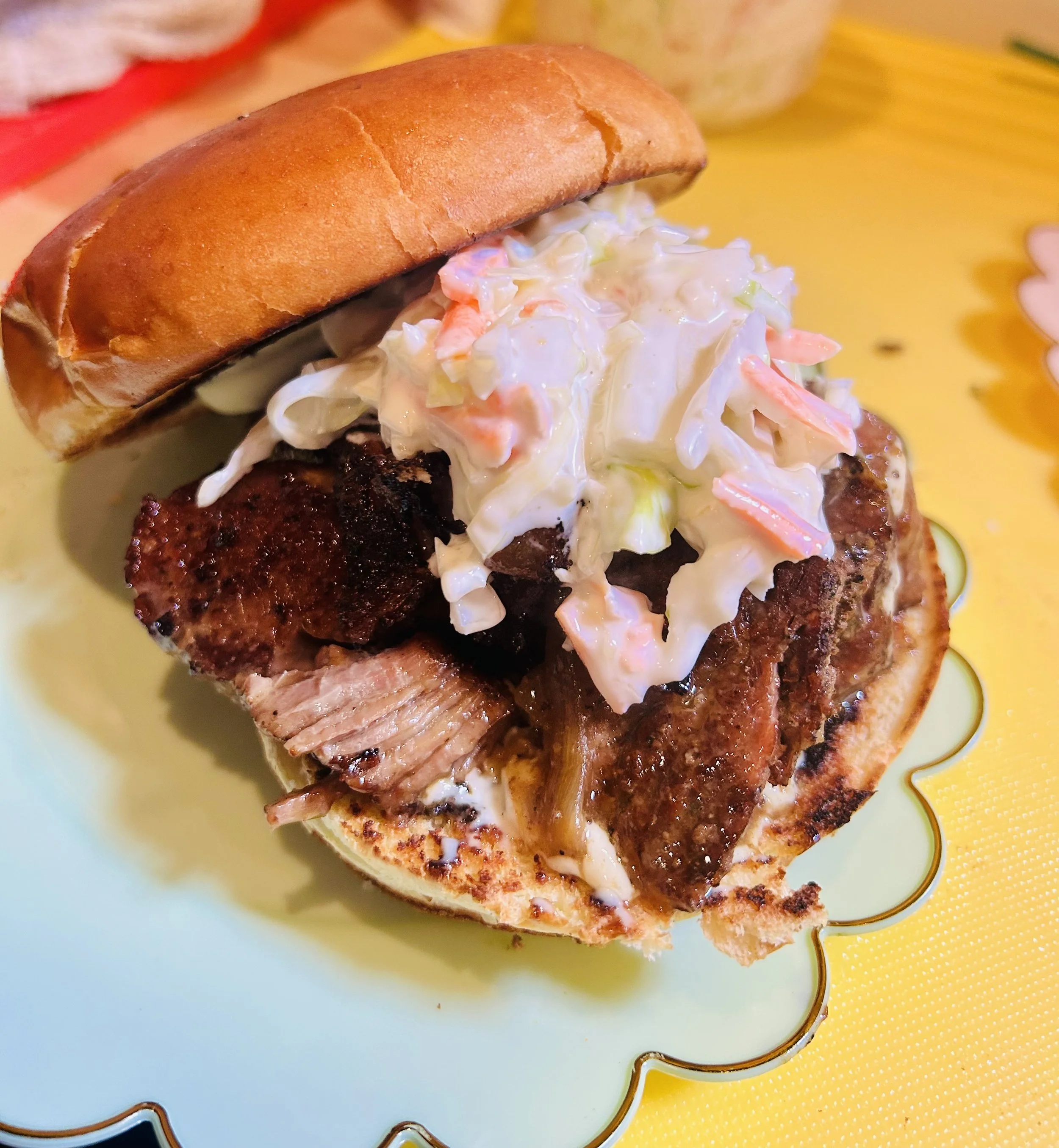 Close-up of a barbecue sandwich with coleslaw on a bun, placed on a decorative plate.