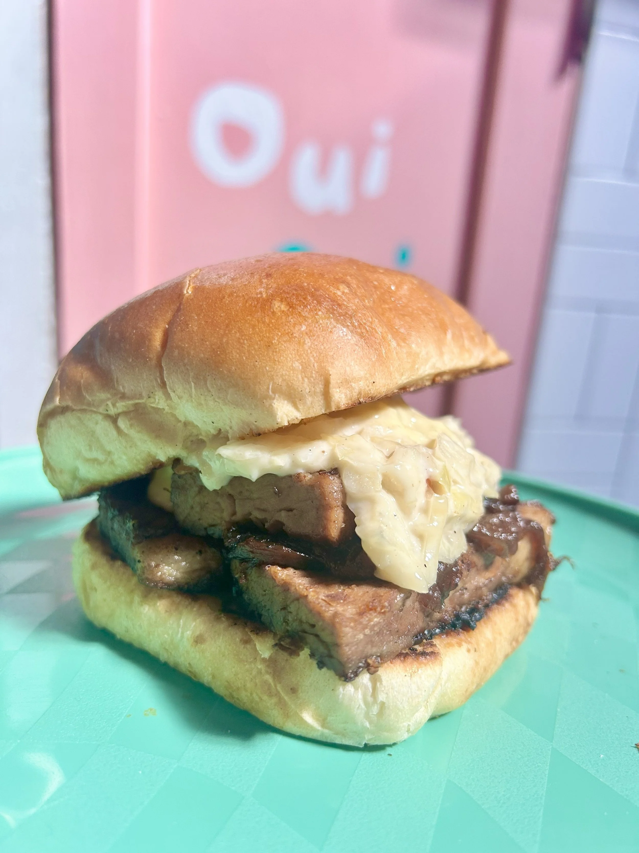 Barbecue sandwich with grilled pork, coleslaw, and bun on a green plate.