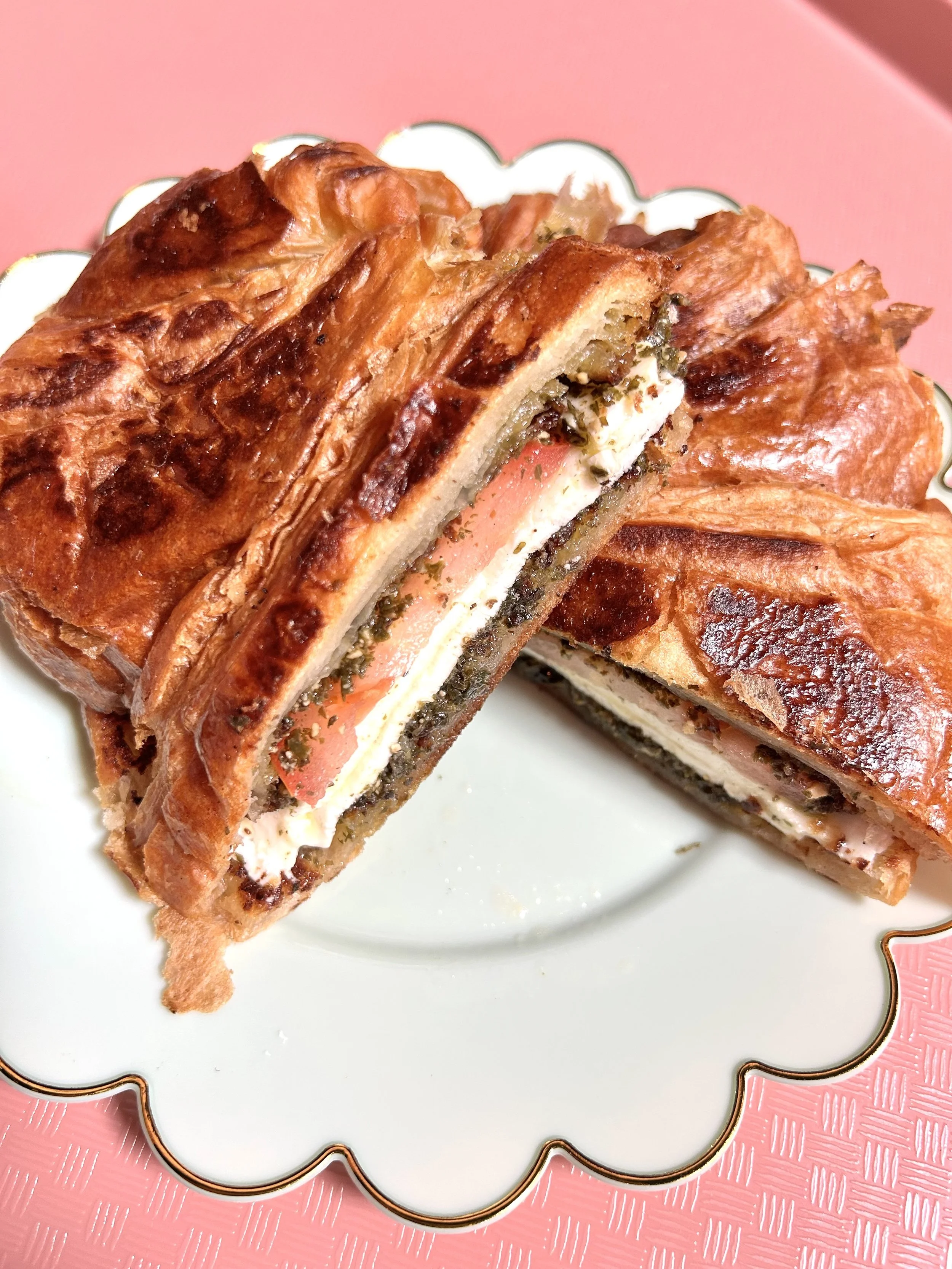 Cross-section of a savory pastry filled with ham, cheese, and herbs, on a decorative white plate.