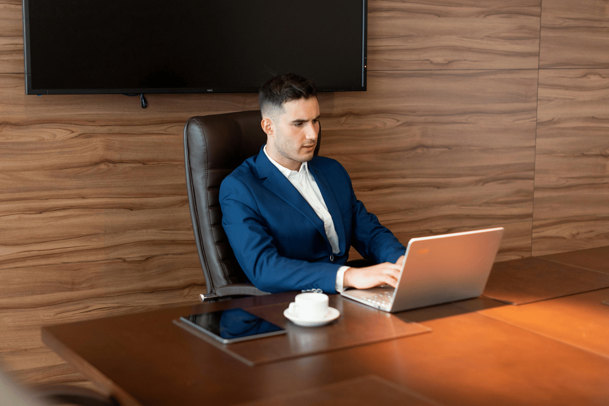 Focused young male executive working on a laptop in a modern wooden office.