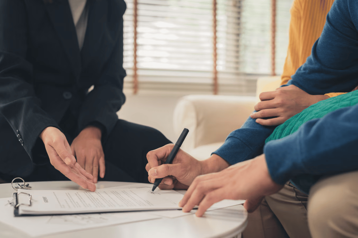 A man signing a contract with two women in a modern office setting.