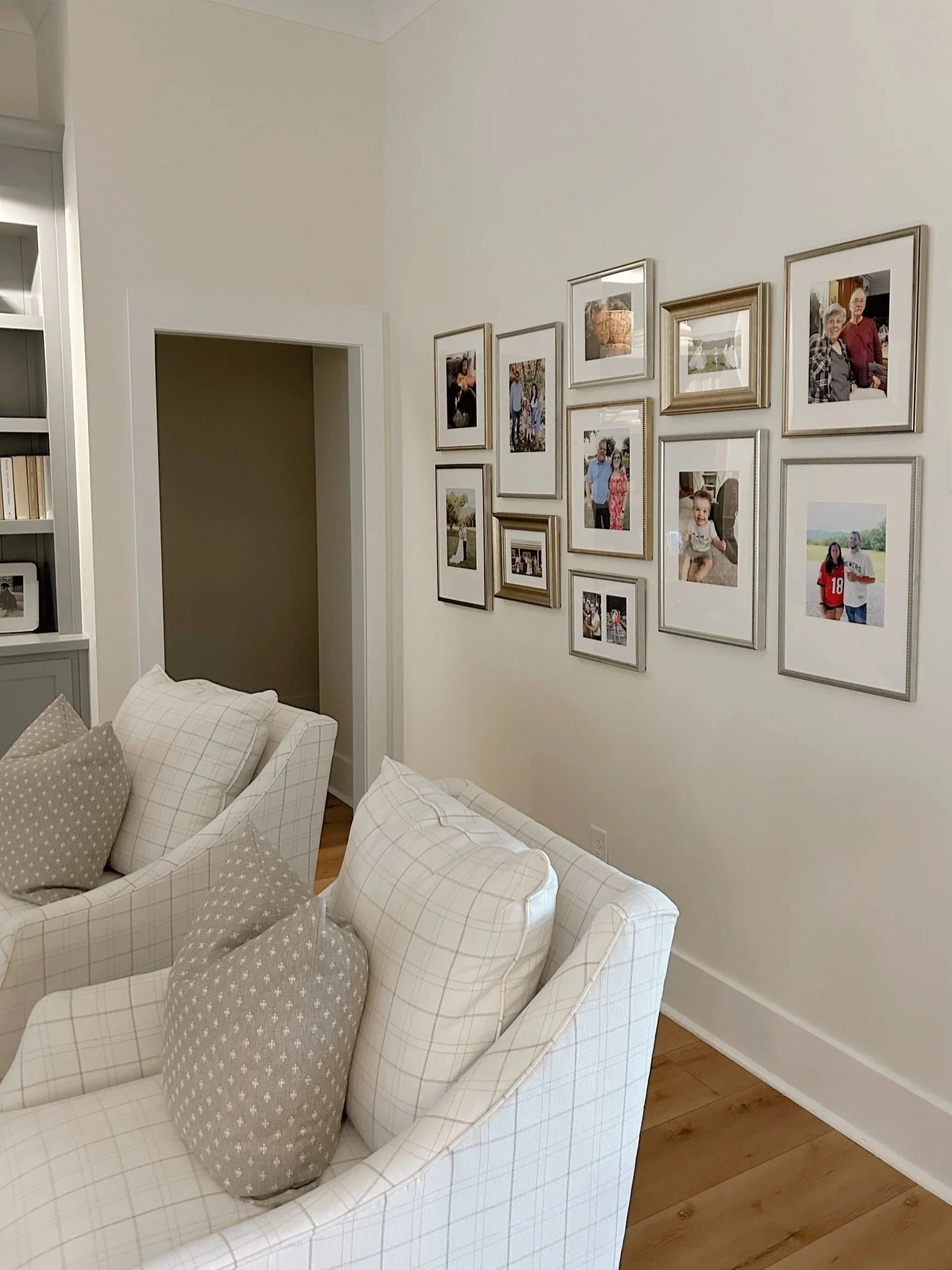 Living room with a white checked sofa, several pillows, and a wall with a gallery of framed family photos.