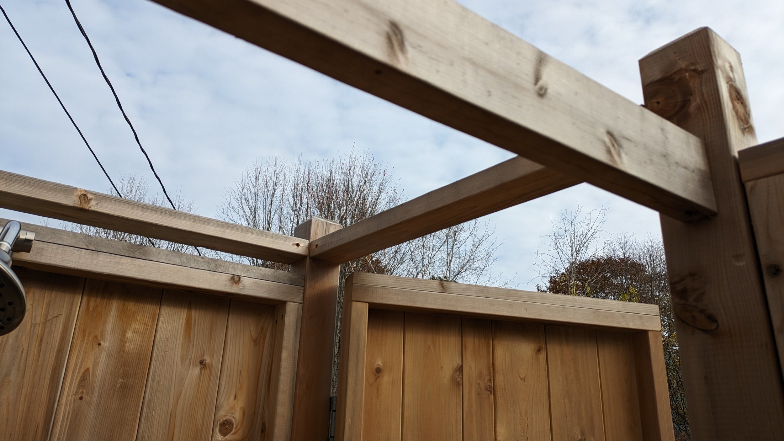 Wooden outdoor fence under construction, with horizontal beams and a partly open gate, view of trees and blue sky in the background.