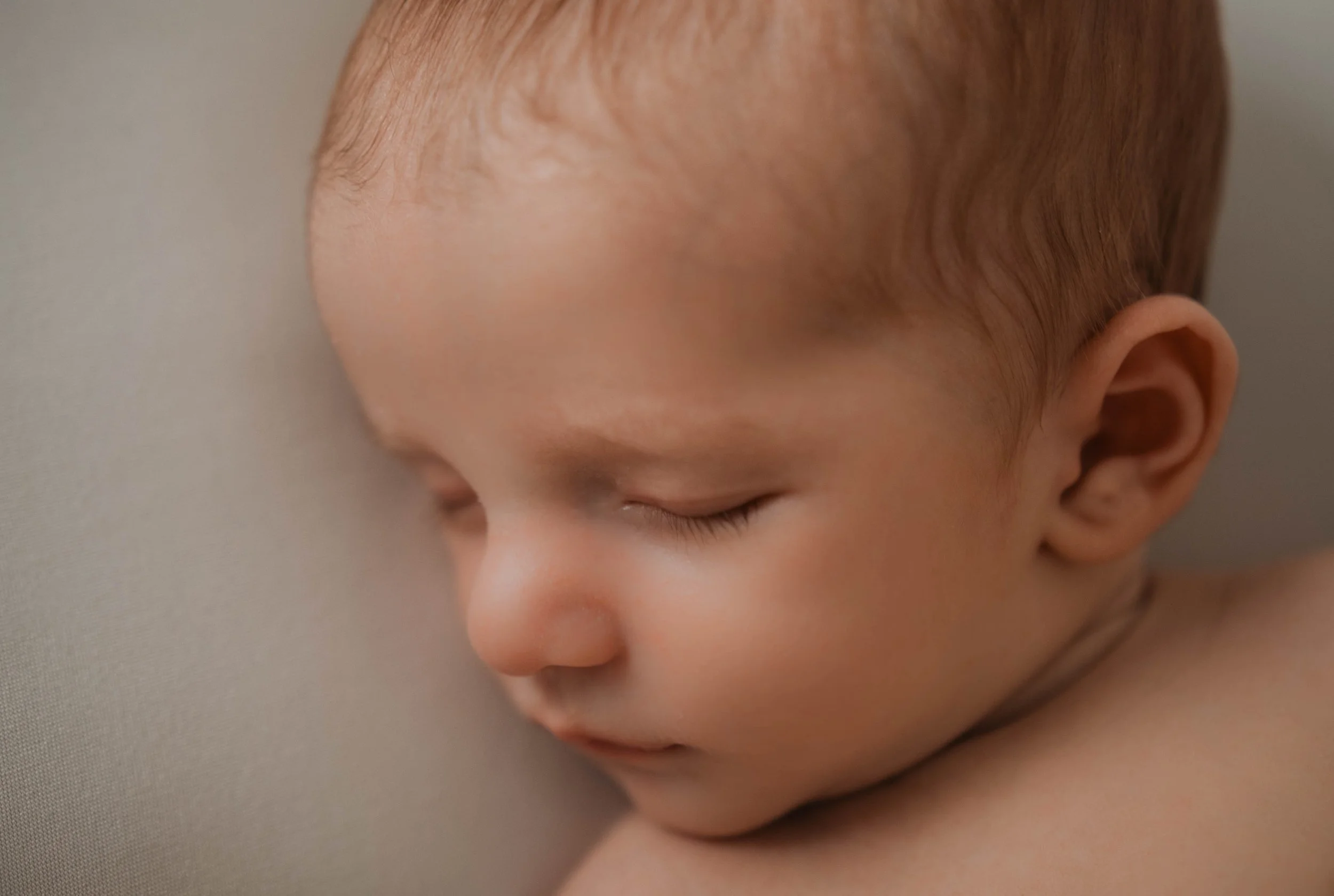 Close-up of a sleeping baby with reddish hair, resting against a soft surface.