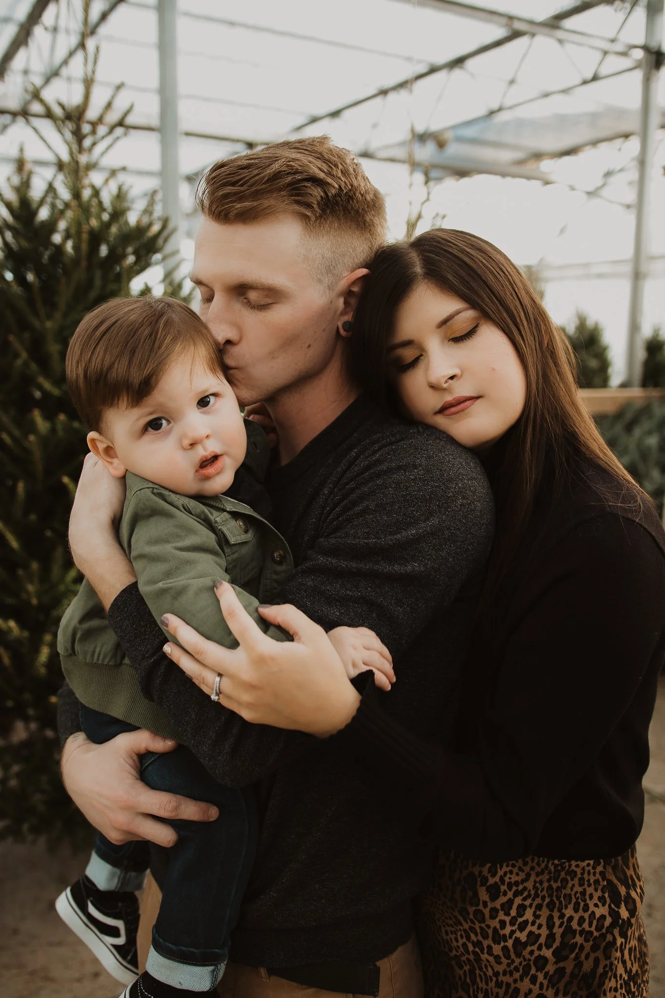 A family of three hugging each other inside a Christmas tree lot.
