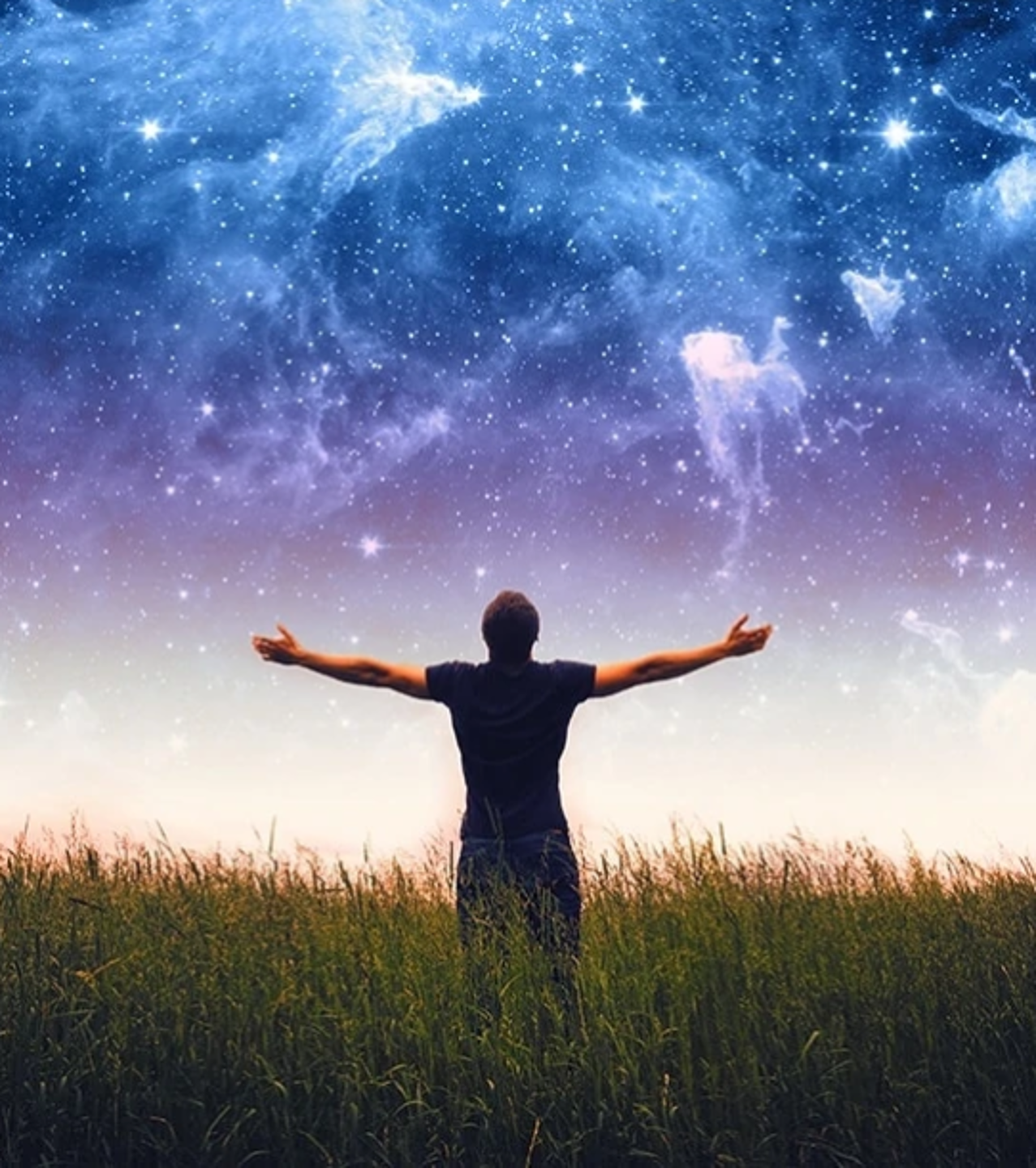Mens staat met uitgestrekte armen in een grasveld en kijkt naar een heldere sterrenhemel en melkweg.