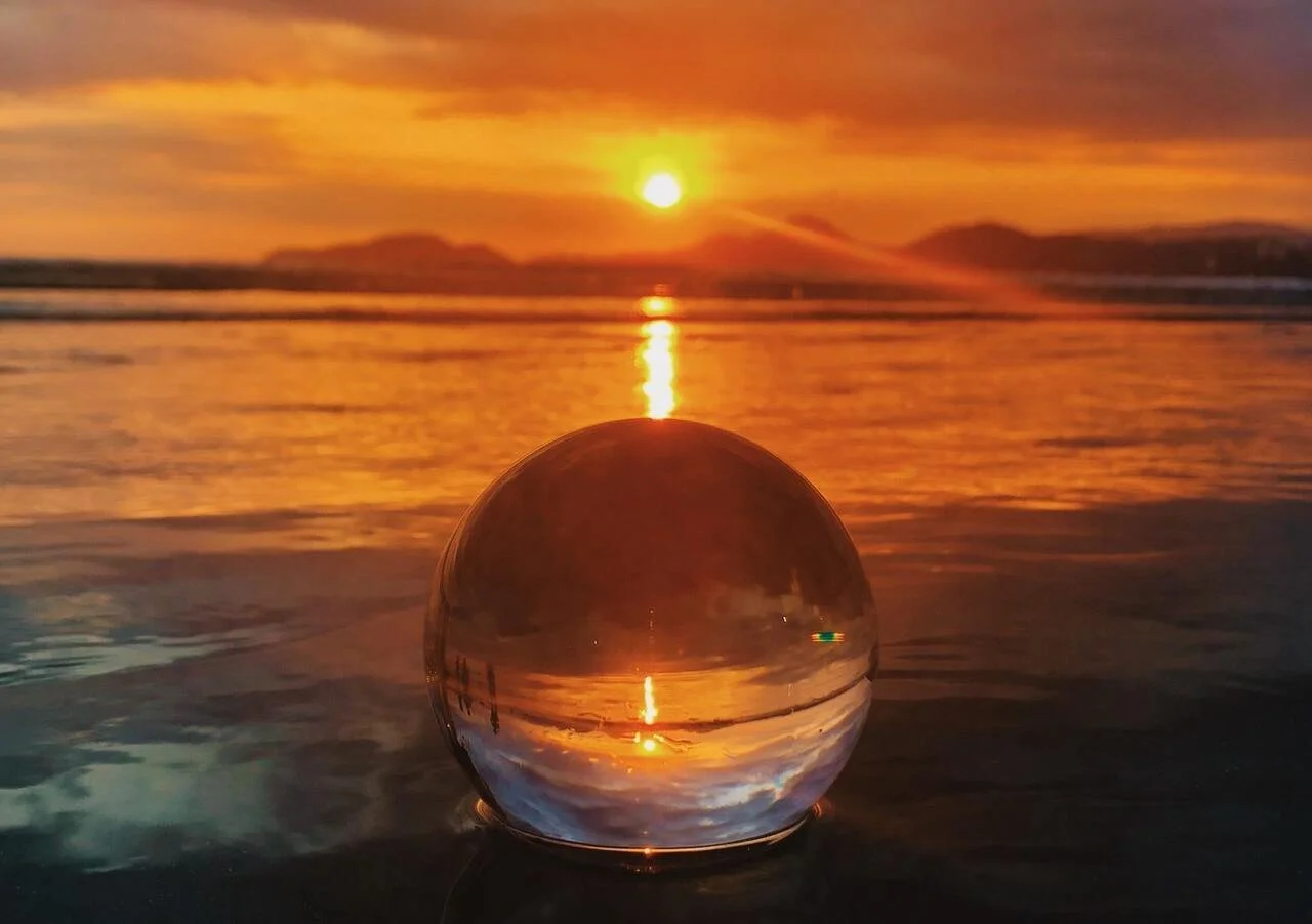 Uitzicht op een zonsondergang over de zee met een glazen bol op de voorgrond die het beeld omkeert.