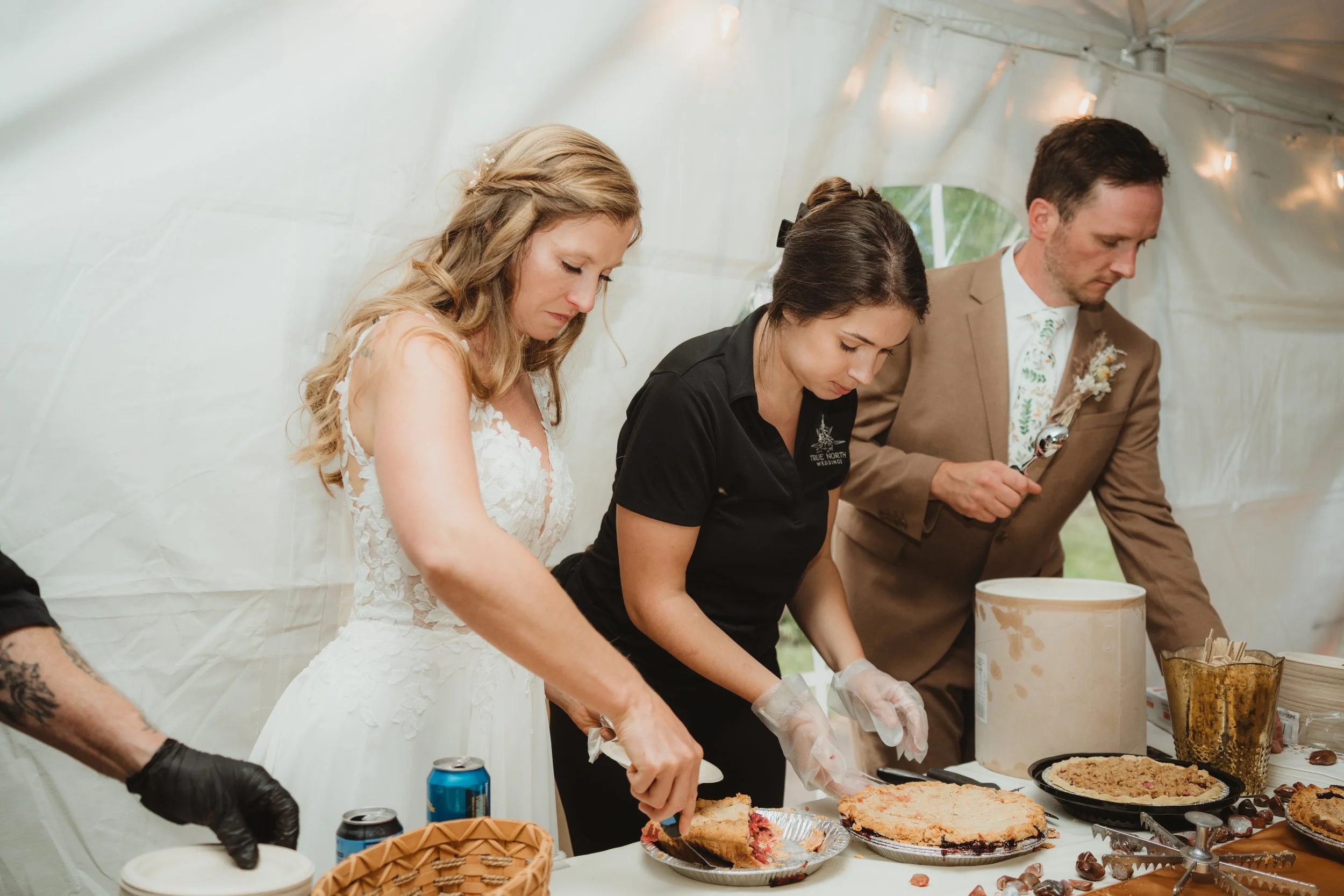 Bride, Gorrm, and a True North Wedding Planner serving cake and pie at the wedding of their dreams. 
