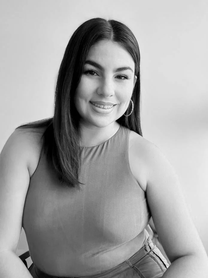 Retrato en blanco y negro de una mujer joven sonriendo, con cabello largo y oscuro, usando un top sin mangas y argollas grandes.