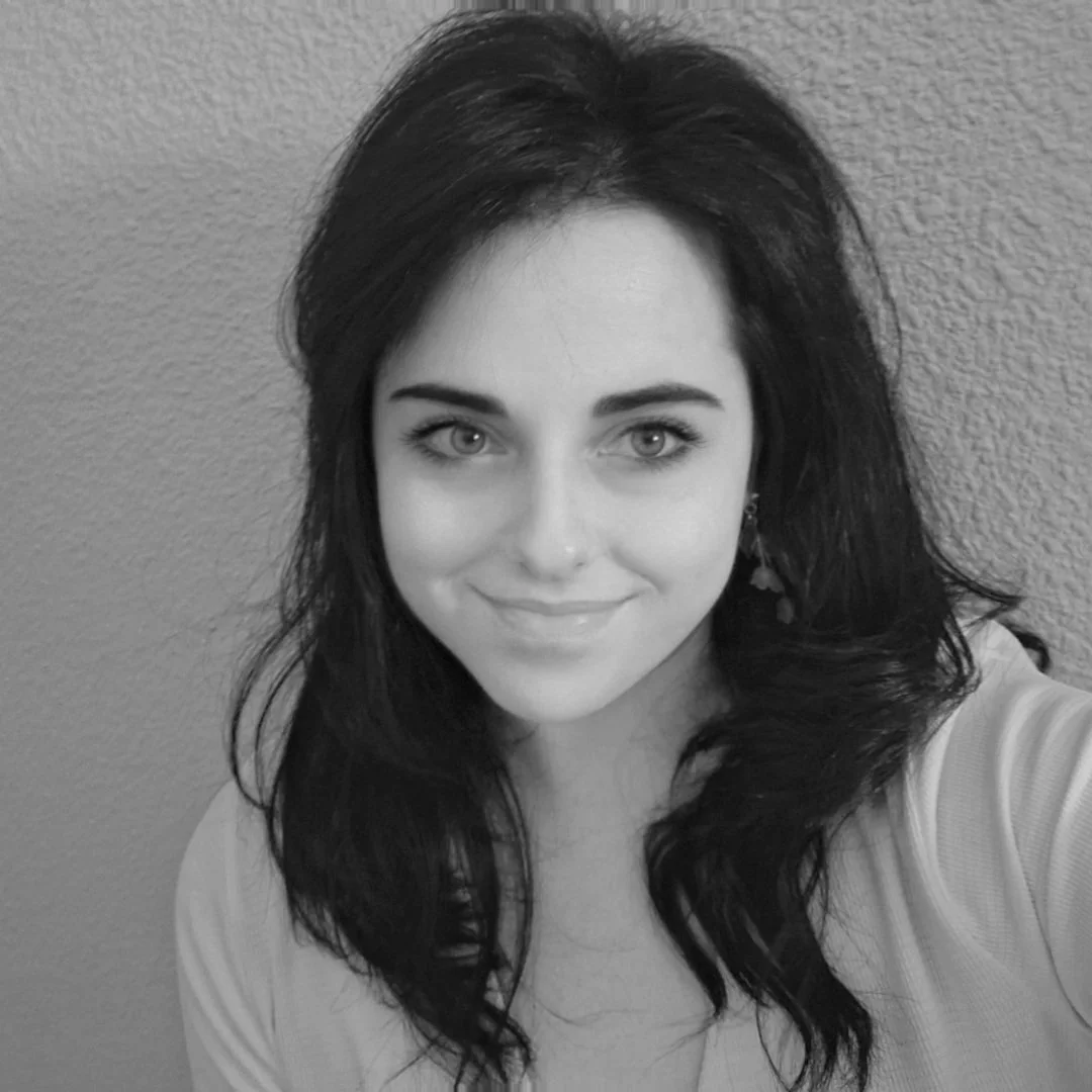 Retrato de una mujer joven con cabello oscuro y largo, sonriendo ligeramente, fondo de pared texturizada.