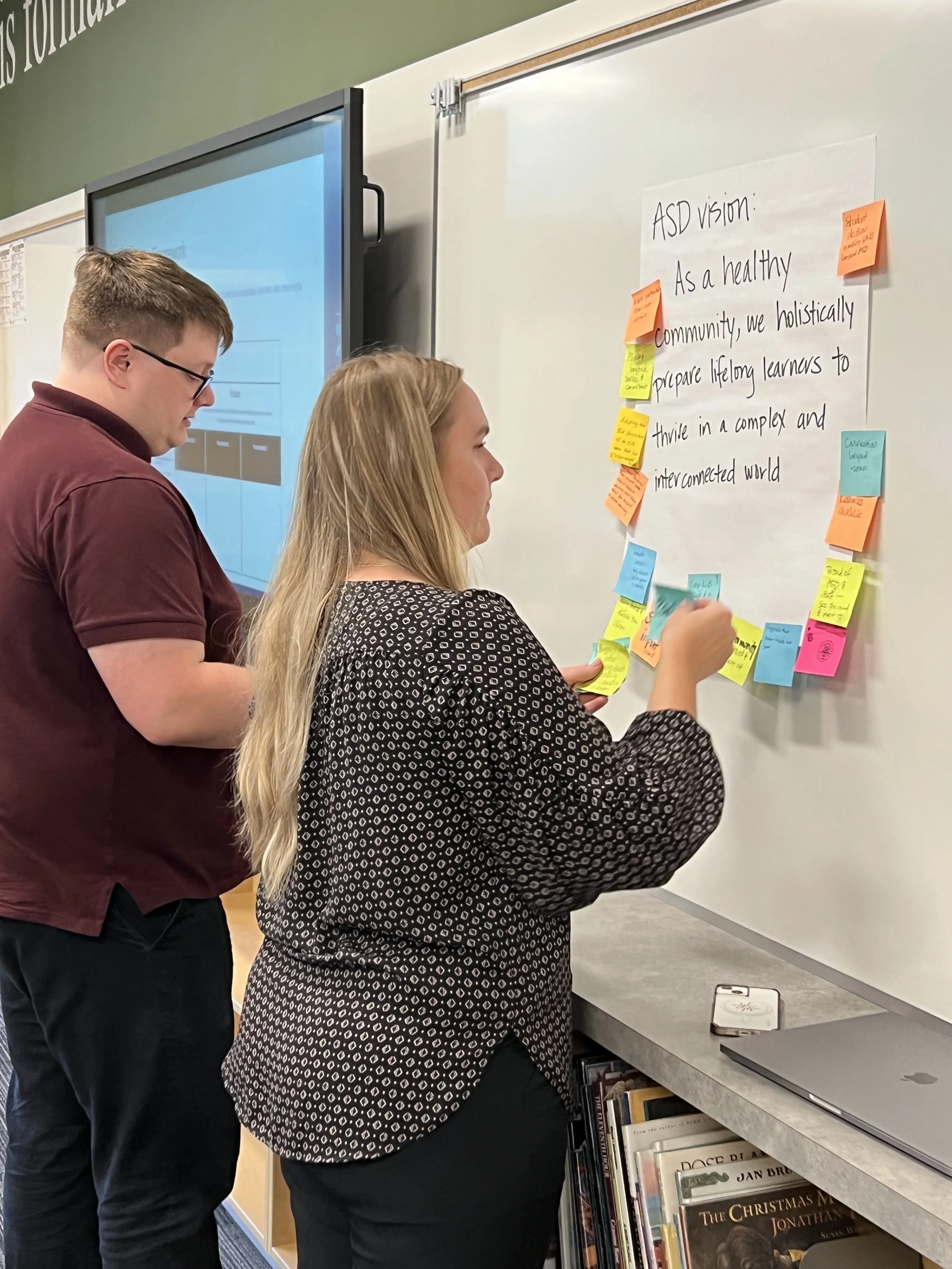 Cadie and Zander adding sticky notes to a poster that reads "ASD Vision"