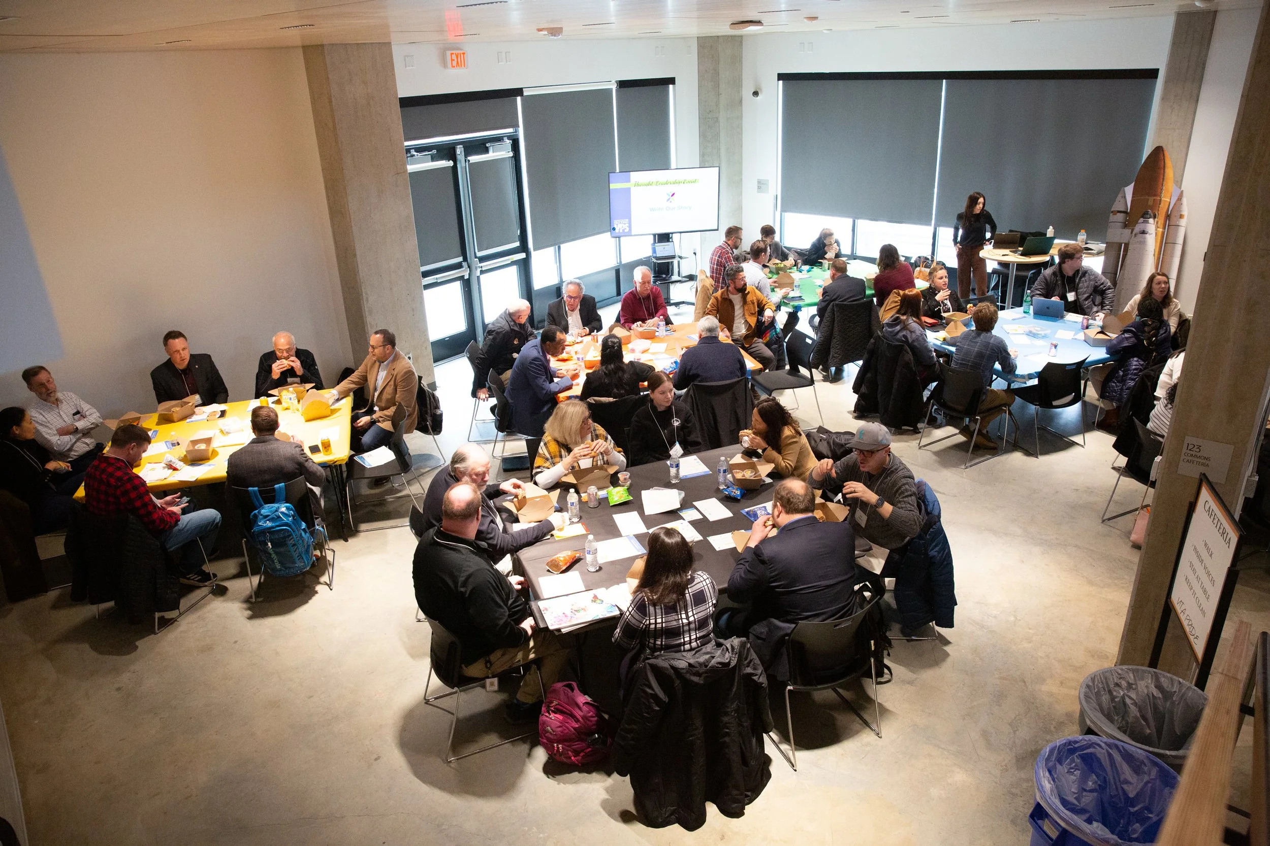 An overhead view of a workshop, with many people sitting at round tables with papers in front of them.