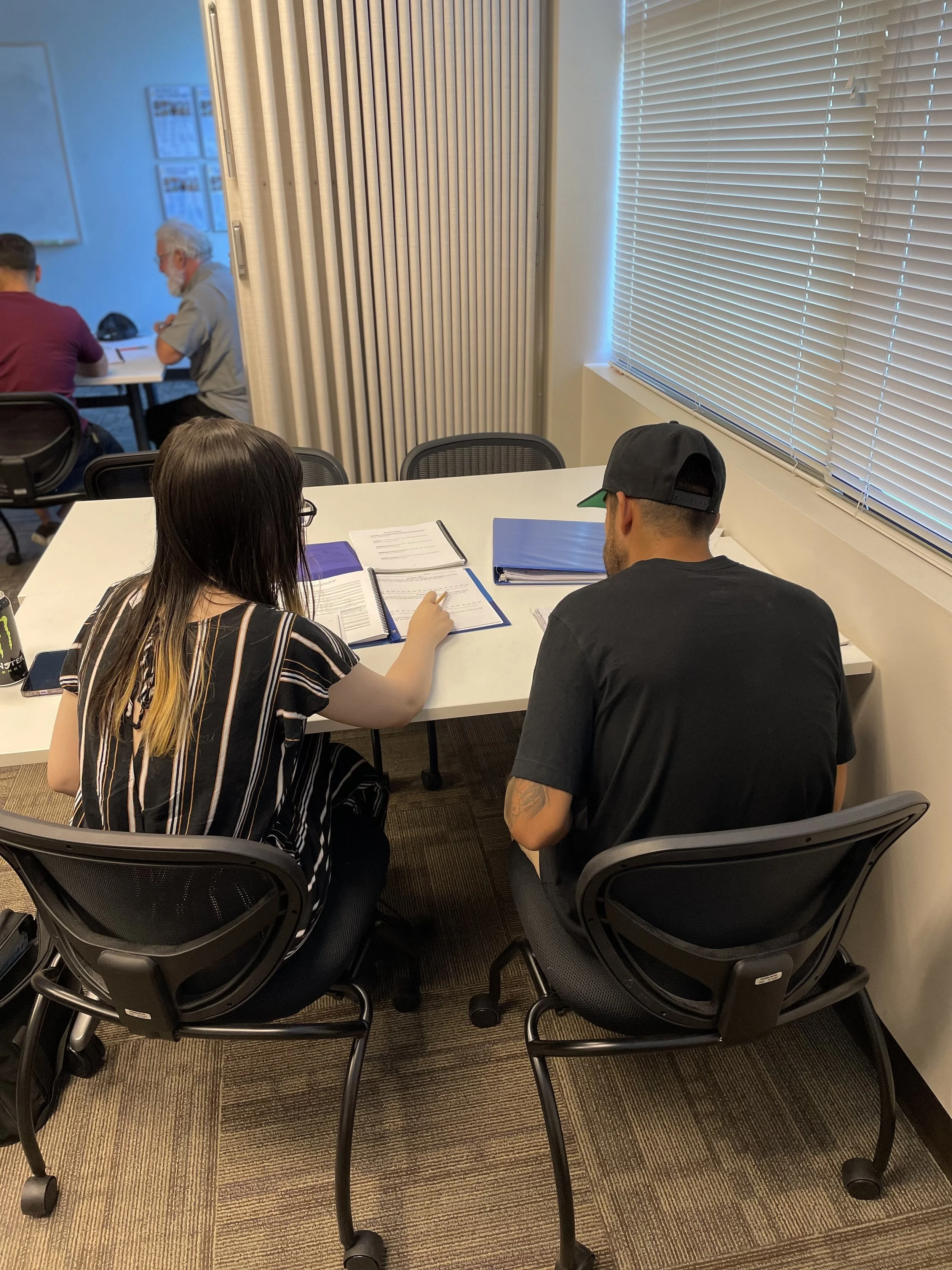 An image of a woman with a striped shirt tutoring a man in a hat