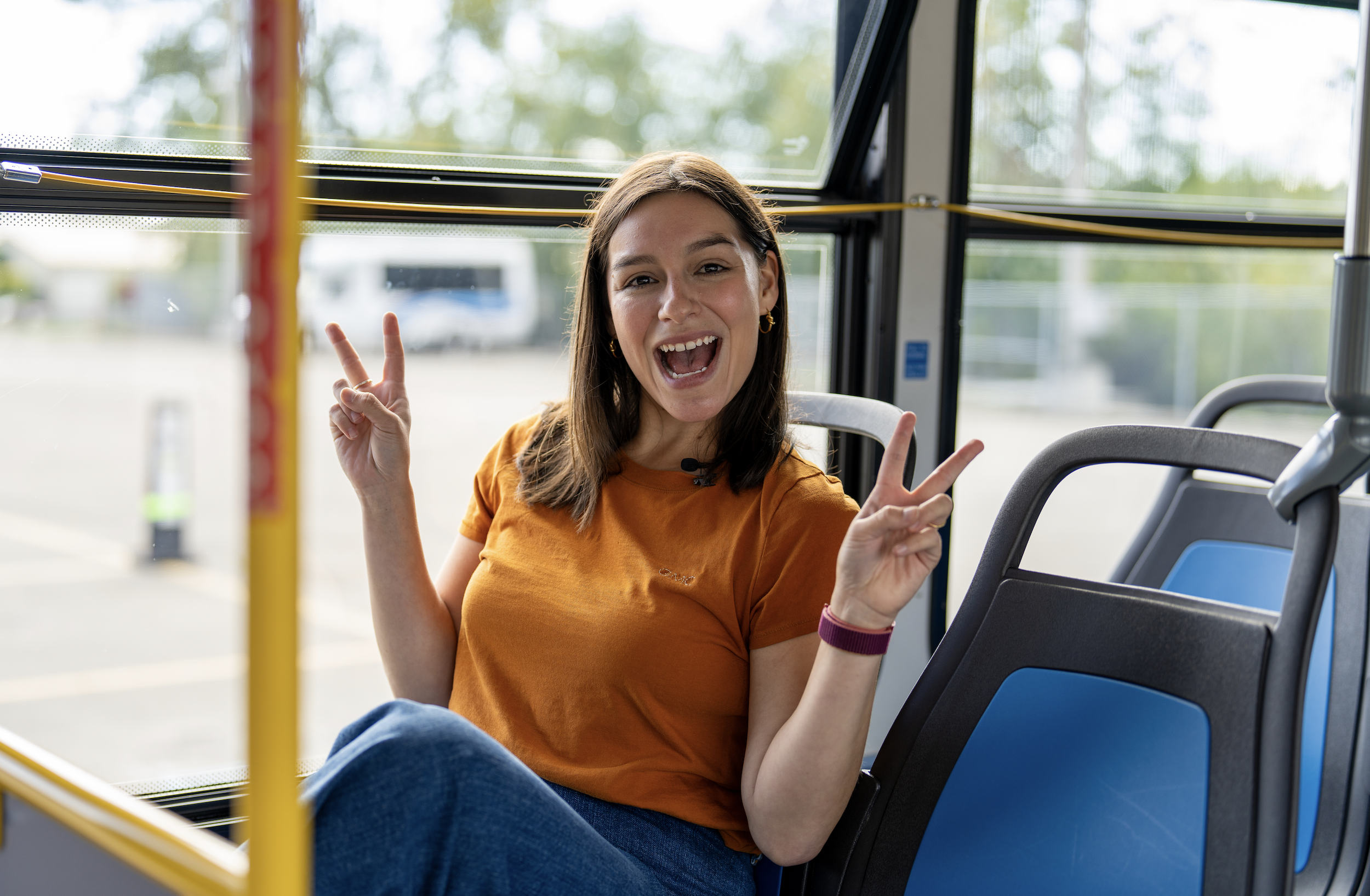 A young woman smiling and holding peace signs up while sitting on the bus