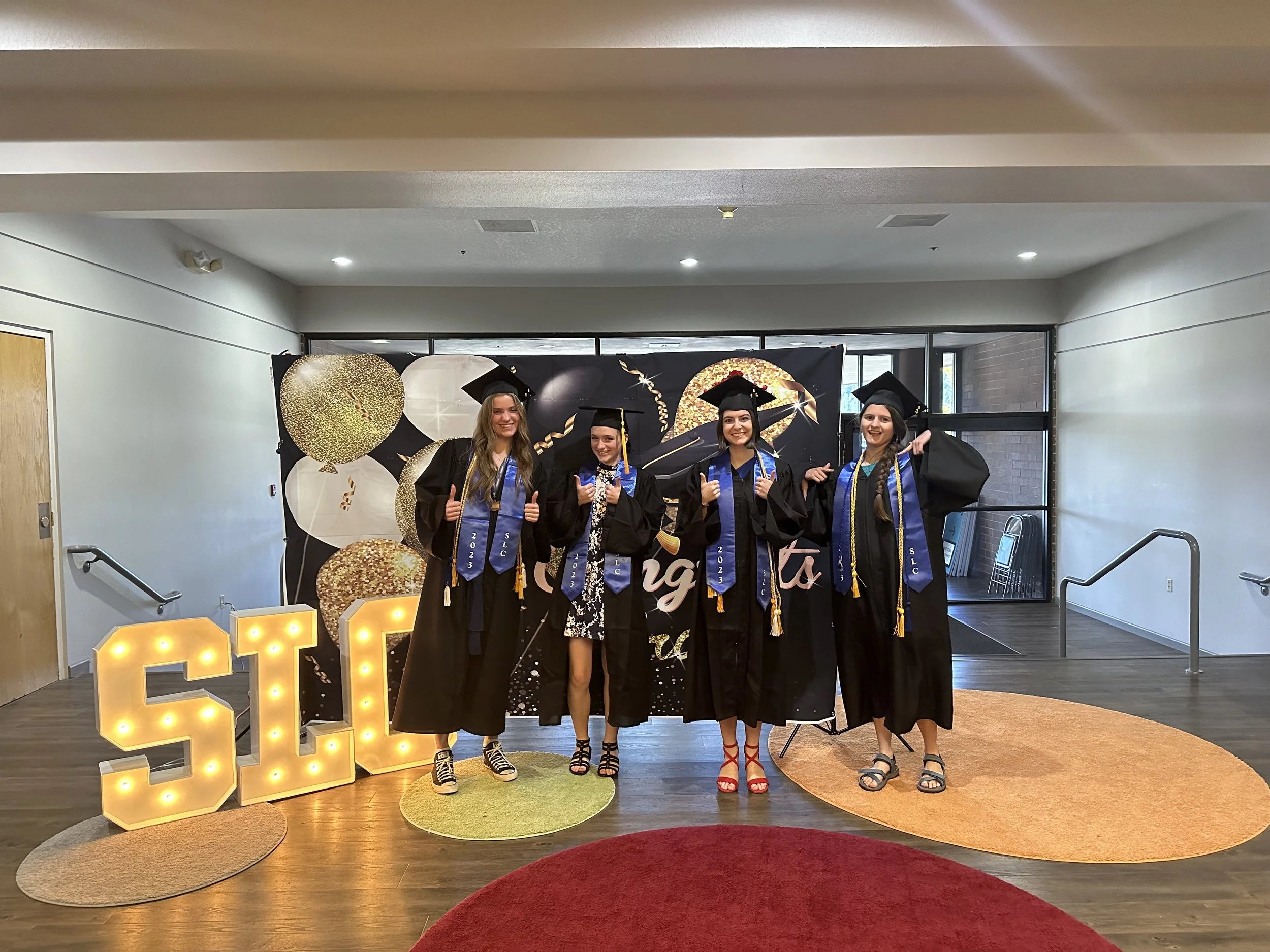 group of 4 graduates posing with thumbs up