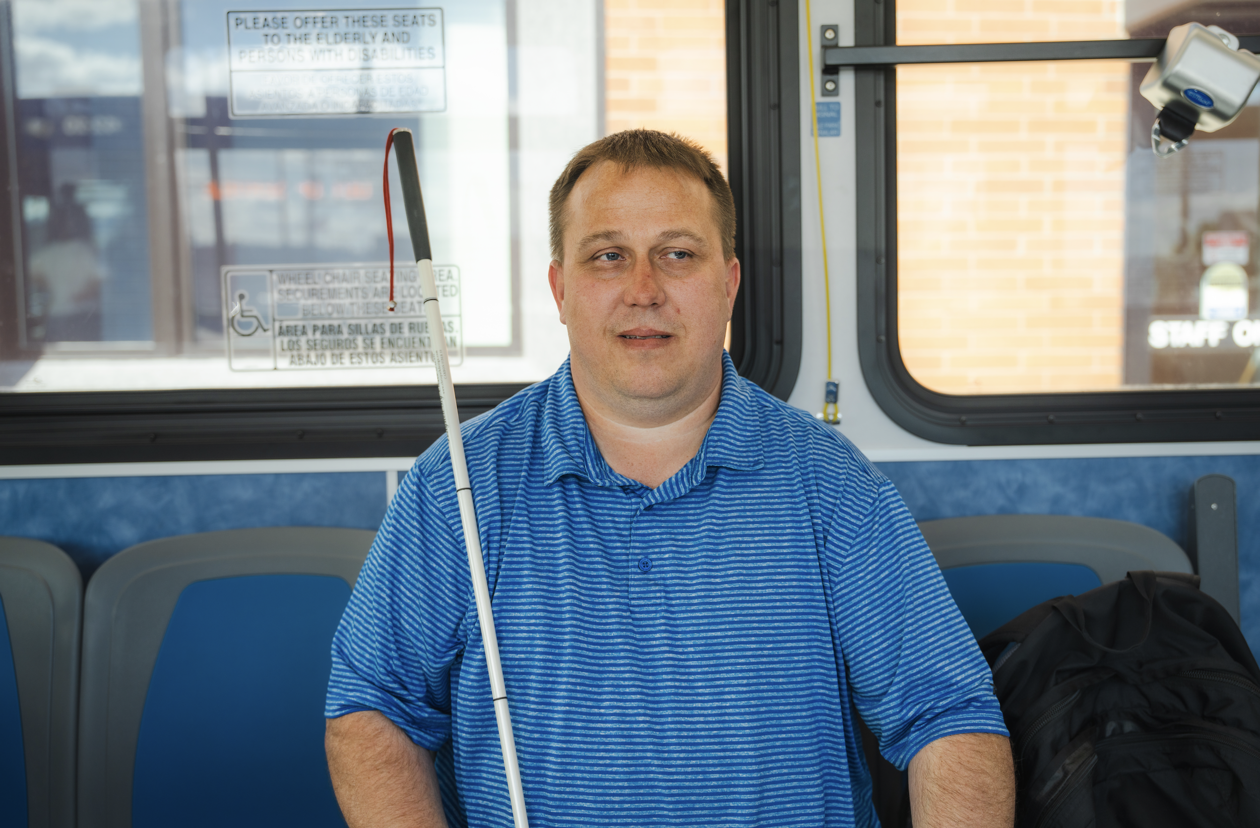 A man sitting with a cane smiling sitting on a bus