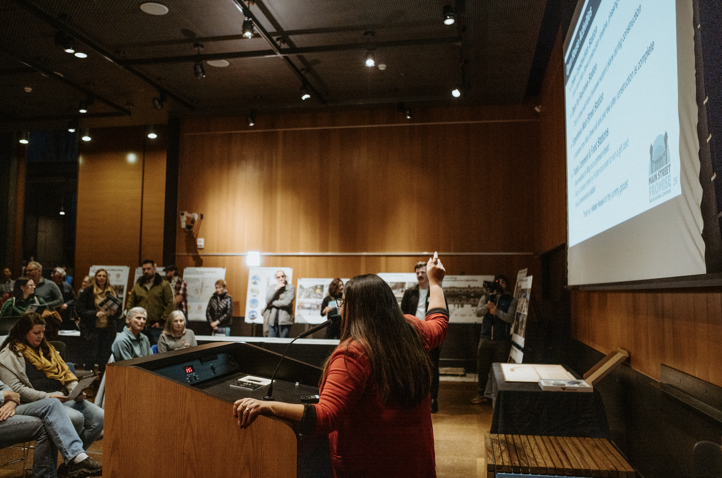 A woman is presenting to a crowd pointing at a screen