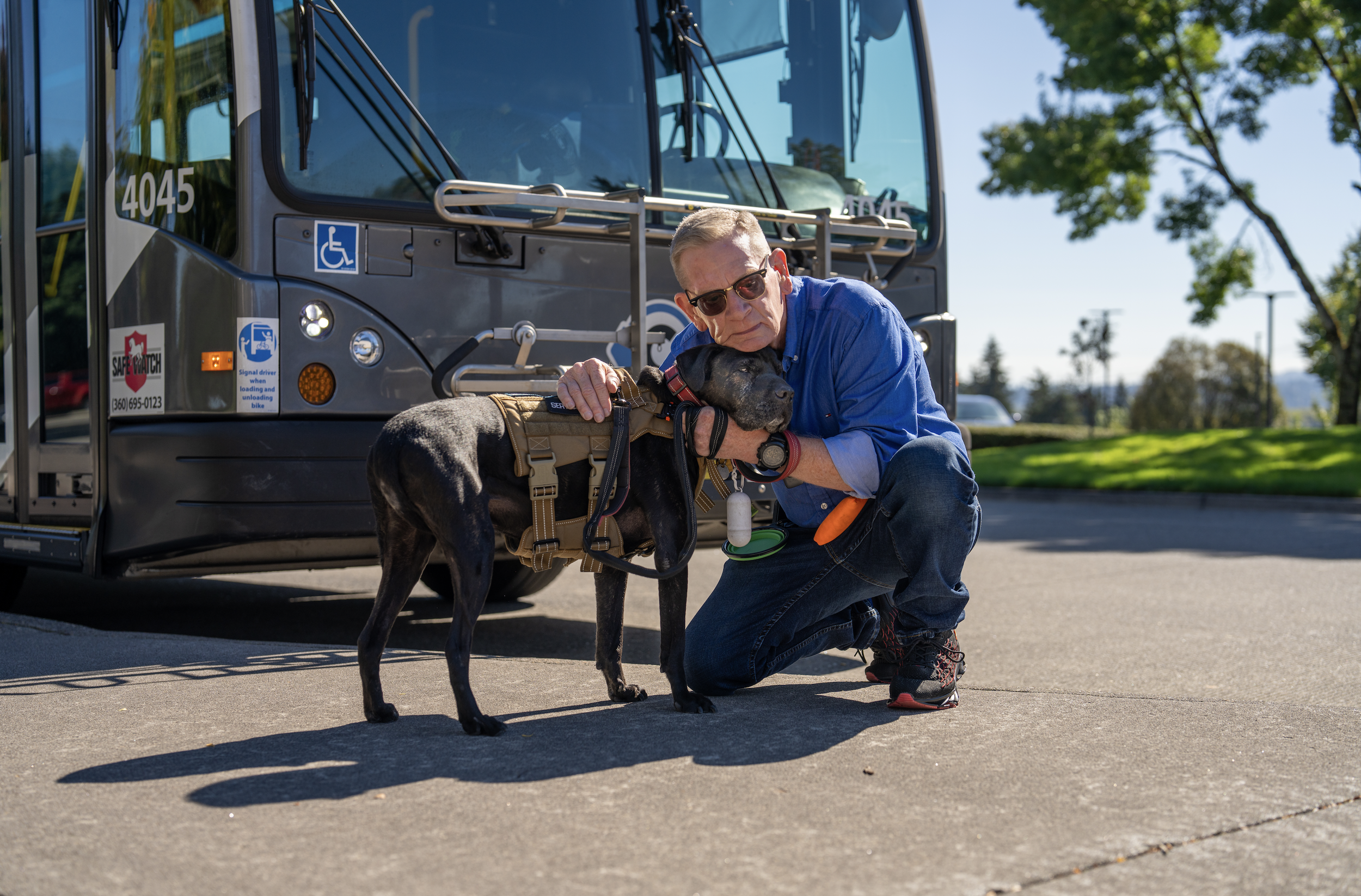 Man leaning over in front of a bus holding his dog