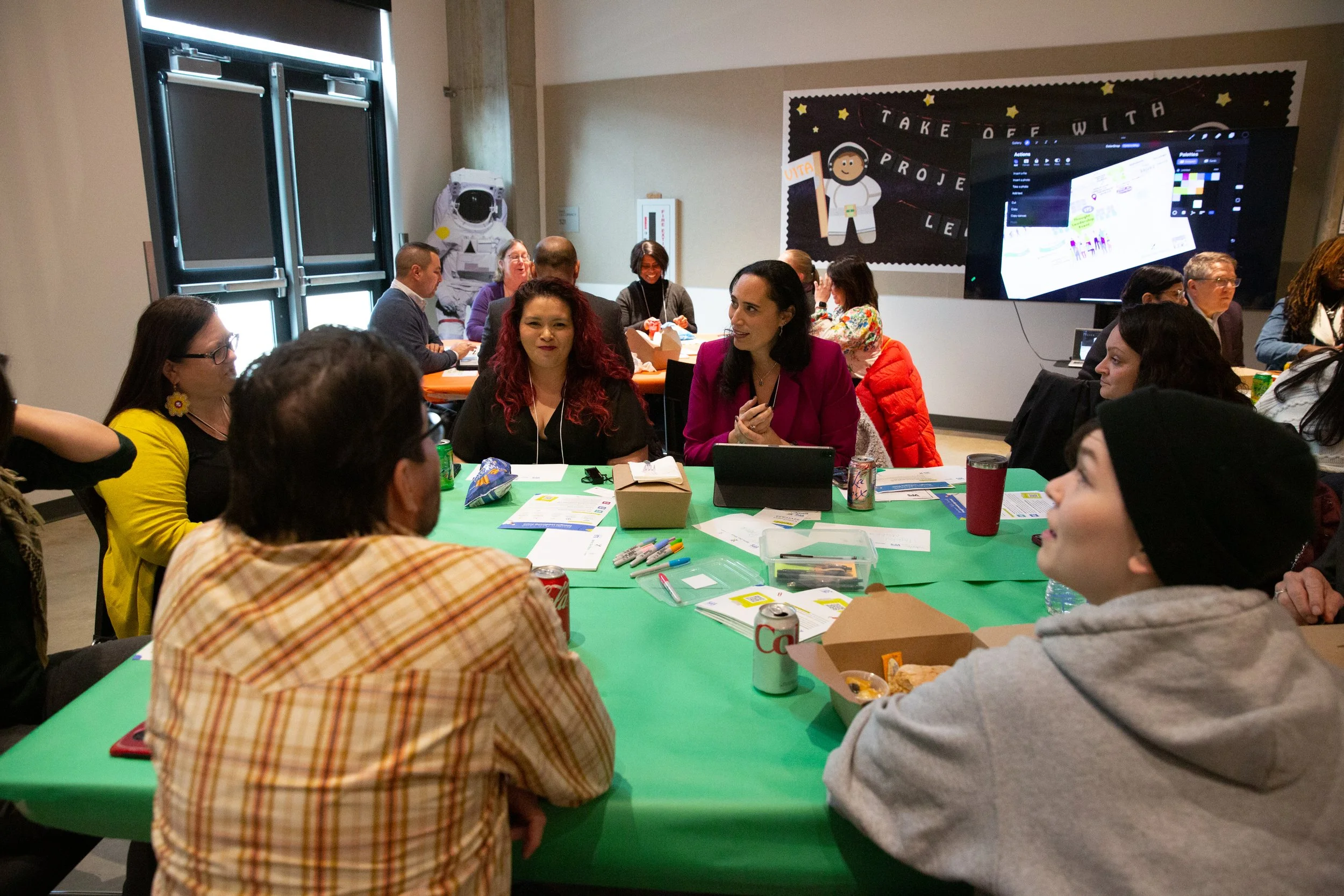 A group of people at a workshop, sitting around a table and talking together.