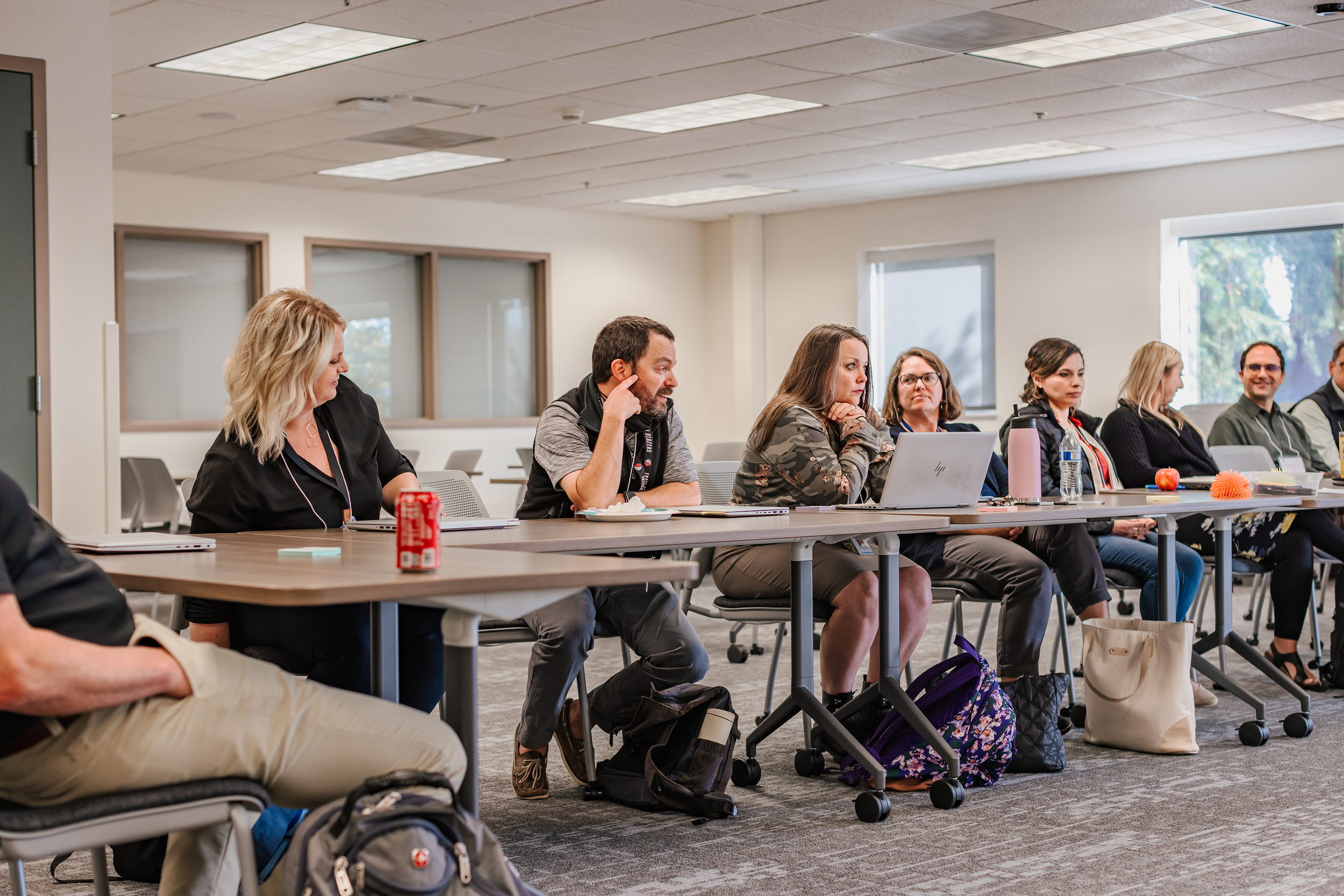 A group of people sitting at desks facing the front of the room, listening to a presenter.