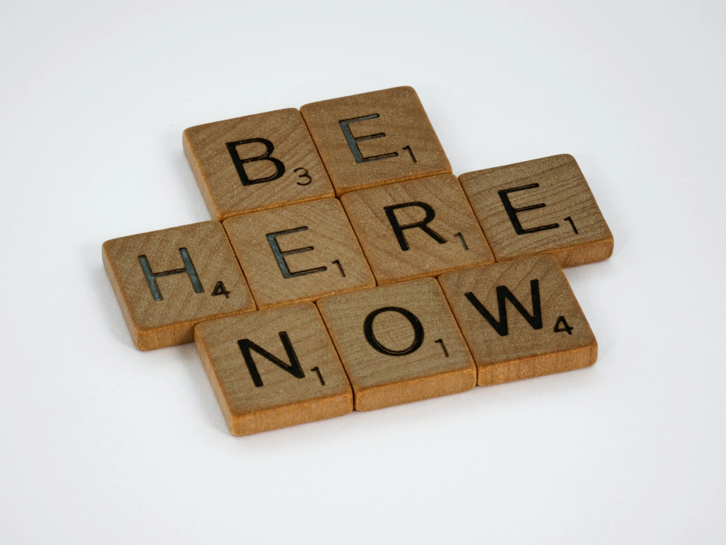 scrabble tiles that spell "Be Here Now"