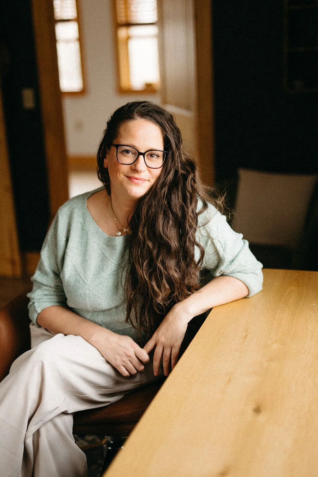 Maggie sits at a wood table, dressed in a green sweater and khaki pants