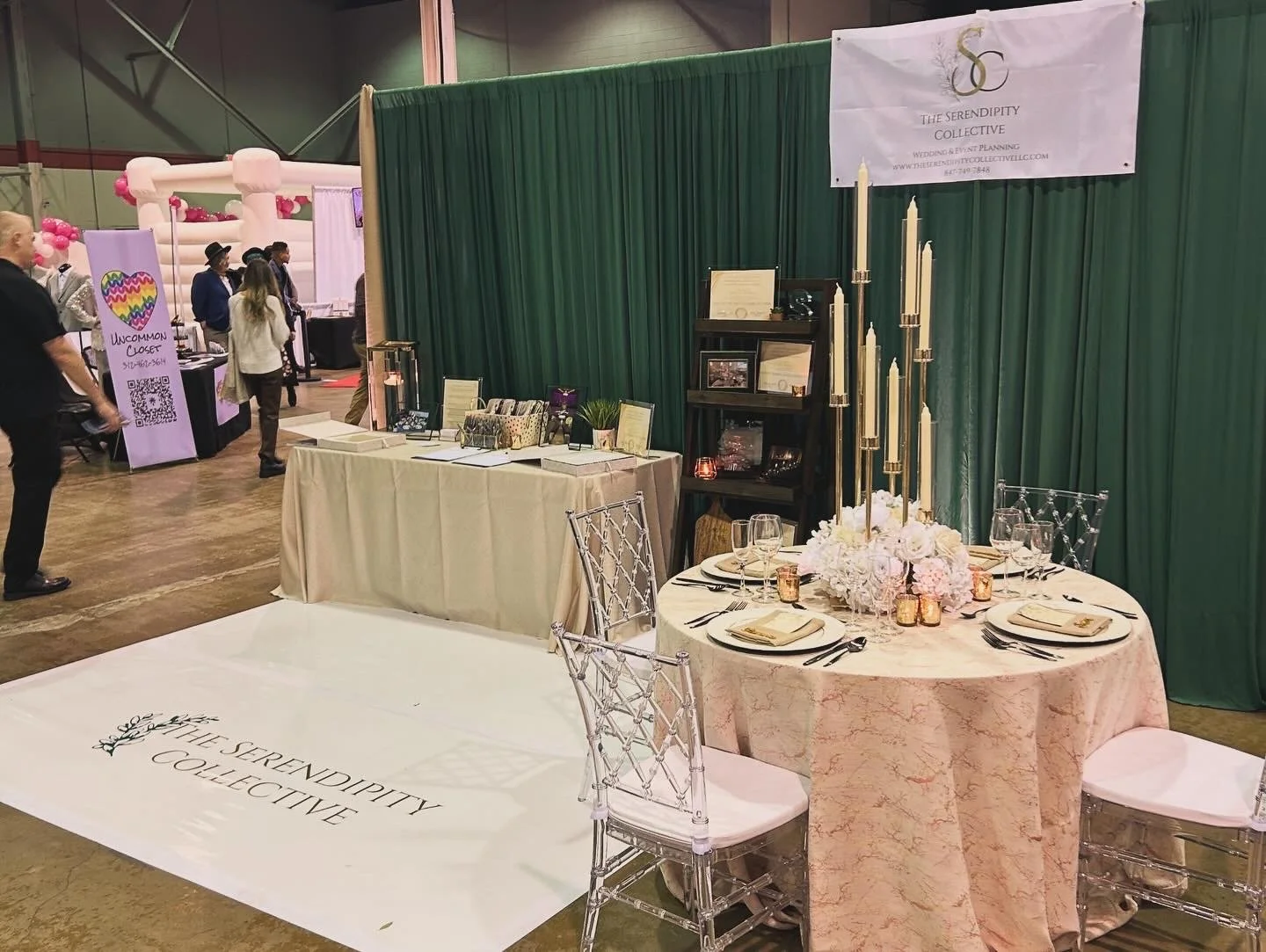 Tradeshow Expo Booth with a round table fully set with flatware and glassware, crystal chivari chairs, chargers, a candelabra centerpice and a vinyl covered dance floor with the logo for The Serendipity Collective