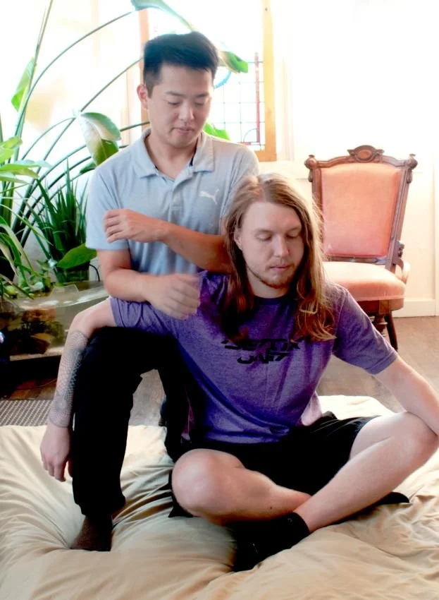 Thai seated massage using forearm and elbows to work along the tops of the shoulder and arm.