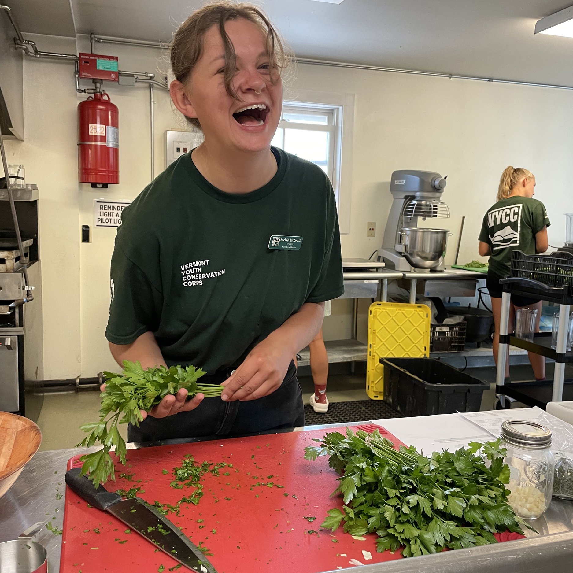 Person laughing while cutting greens in an industrial kitchen.