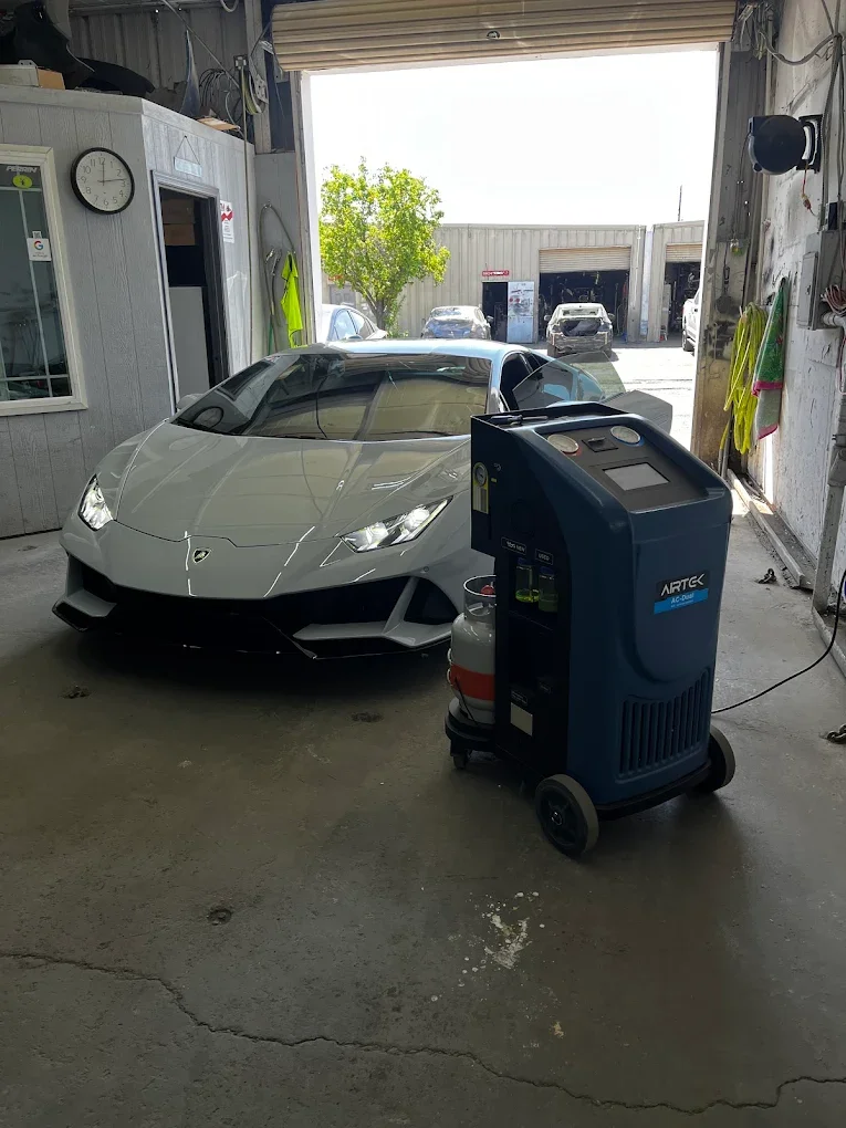 Gray Lamborghini sports car inside a garage with an open large garage door, with cars and a tree visible outside.