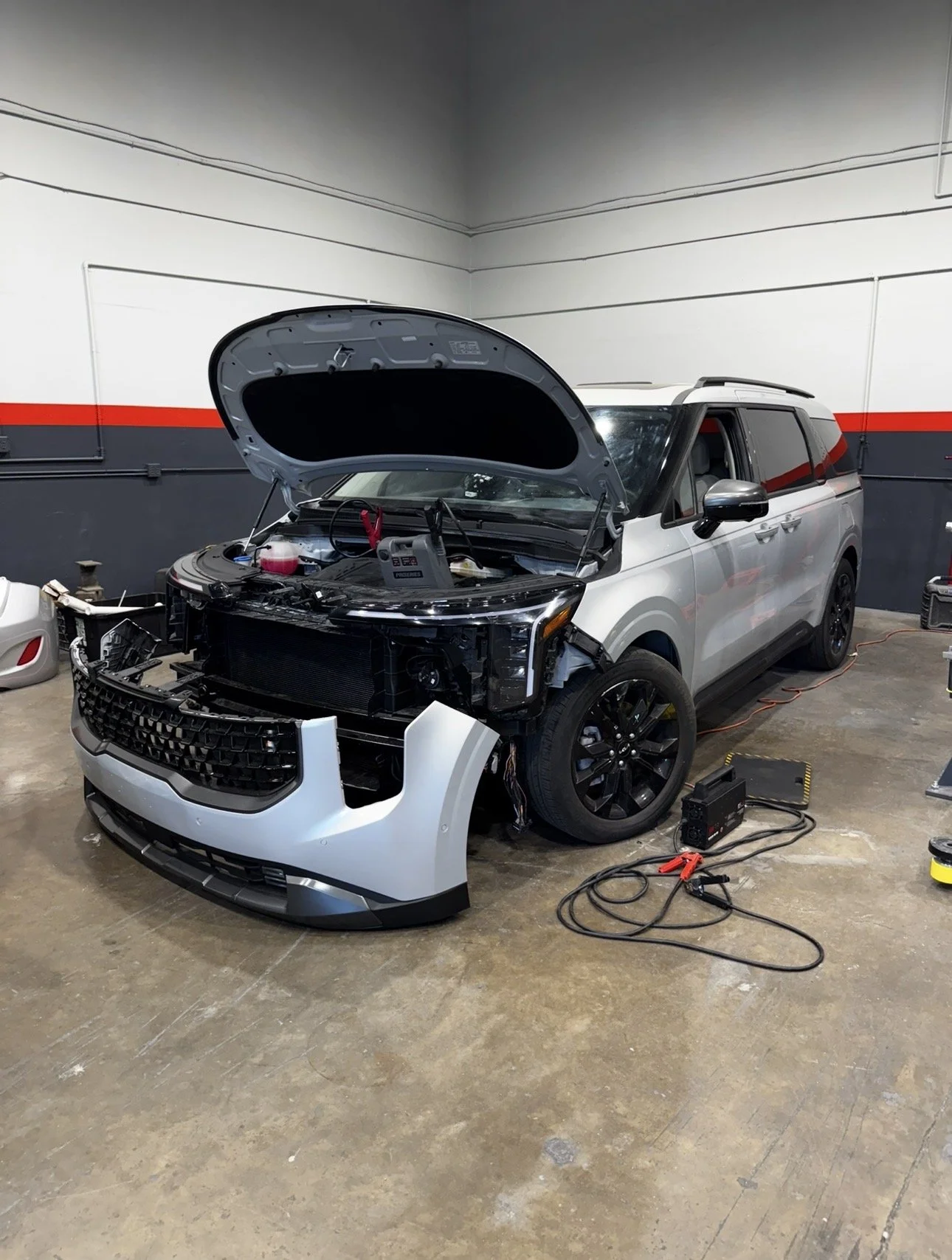 A car undergoing restoration or repair in a garage, with the driver's side door removed and masked edges around the window opening for painting or sealing.