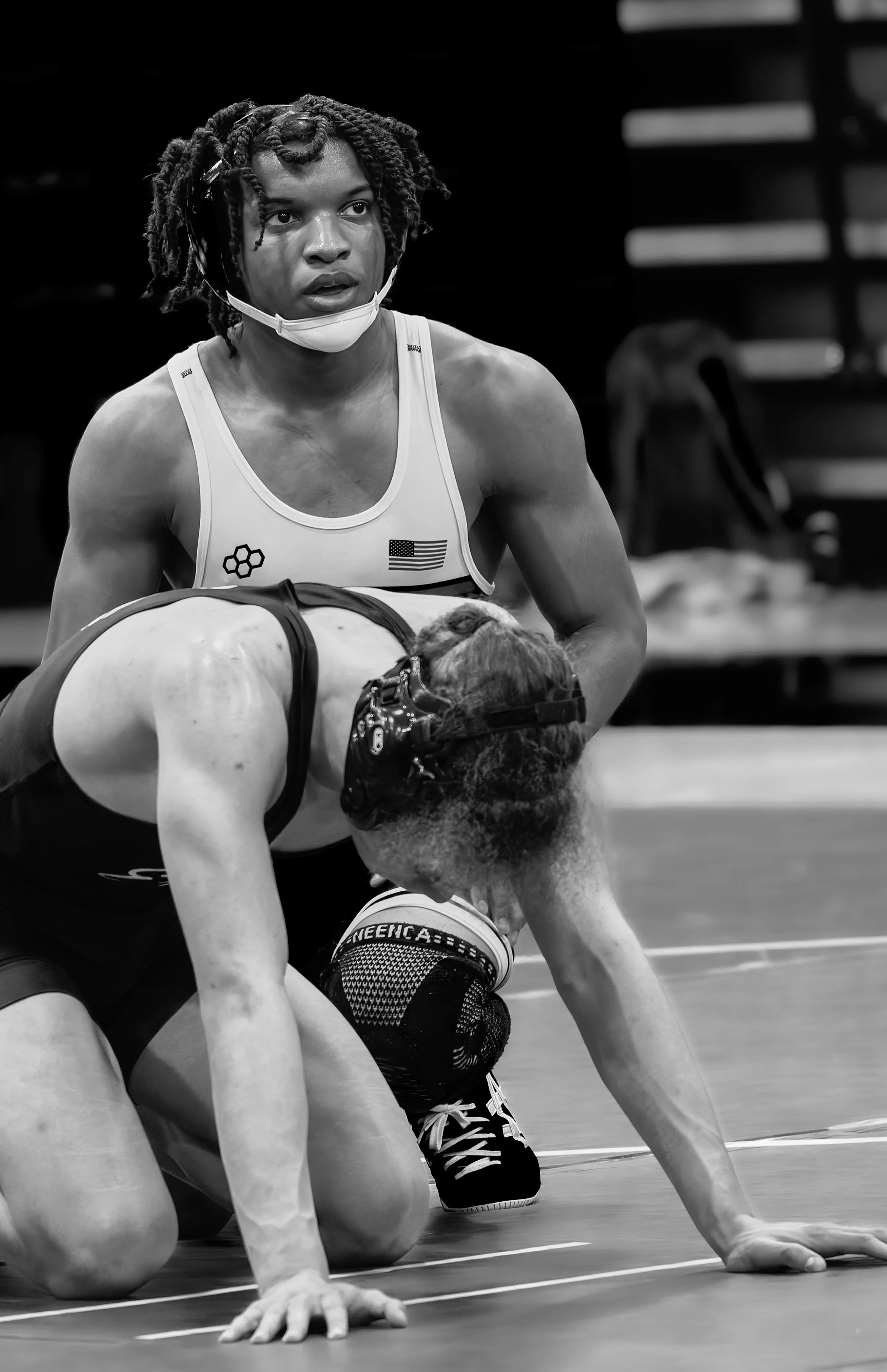 Two female wrestlers competing on mat, one woman wearing a sports bra with American flag and another with a headgear, in a black and white photo.