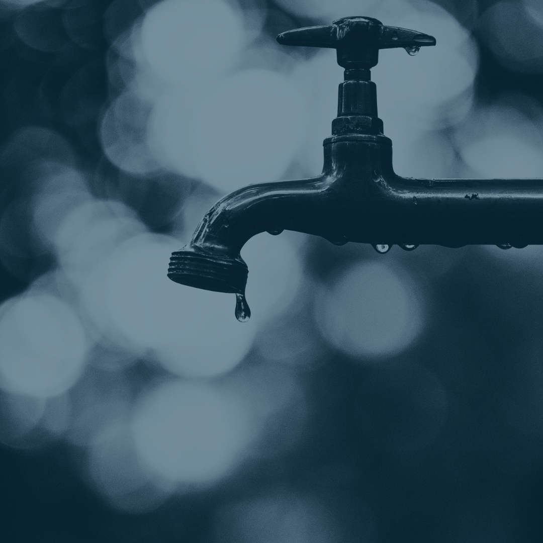 A close-up of a black outdoor water faucet with a single water droplet hanging from its spout, blurred background with circular bokeh lights.