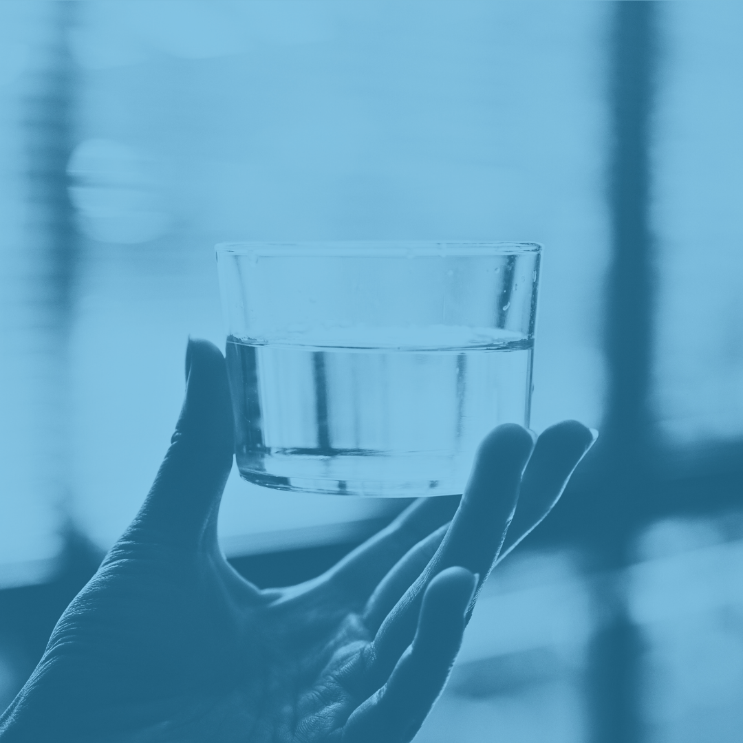 Hand holding a glass of water against a blurred background.