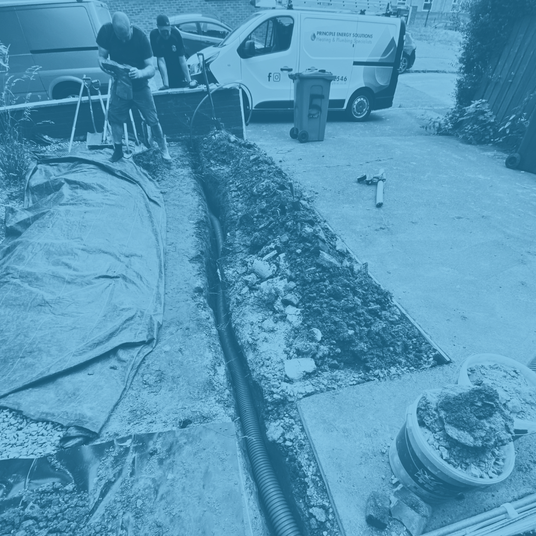 Workers installing underground utility pipes in a trench next to a parking lot, with construction tools and equipment nearby.