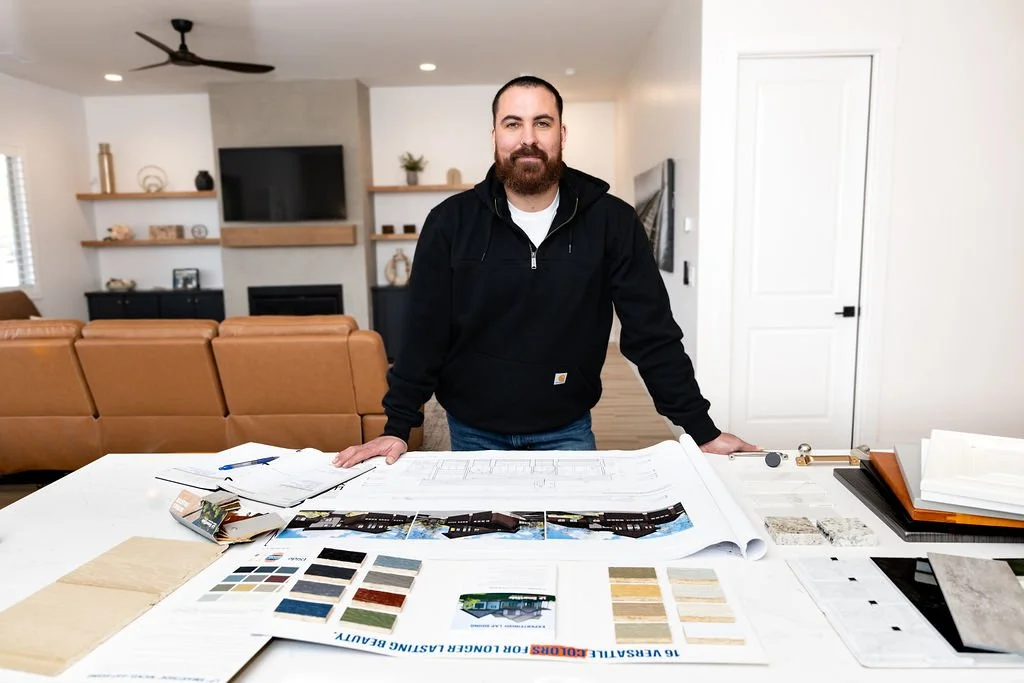 A man standing at a table with architectural plans and color samples in a modern living room.