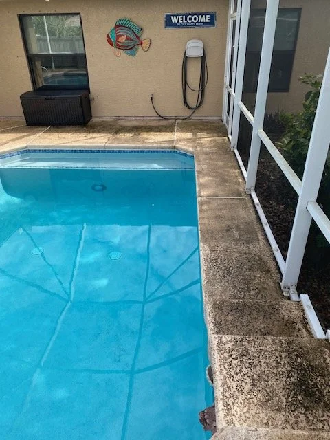 Swimming pool with a concrete deck, enclosed patio, decorated wall with fish artwork, and a welcome sign.
