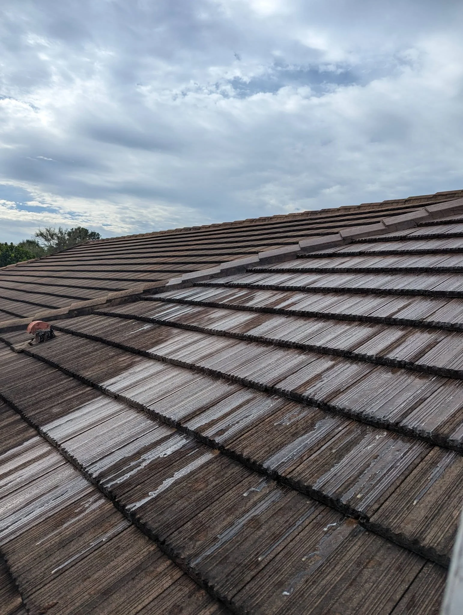 A view of a sloped rooftop with brown tiles under a partly cloudy sky.