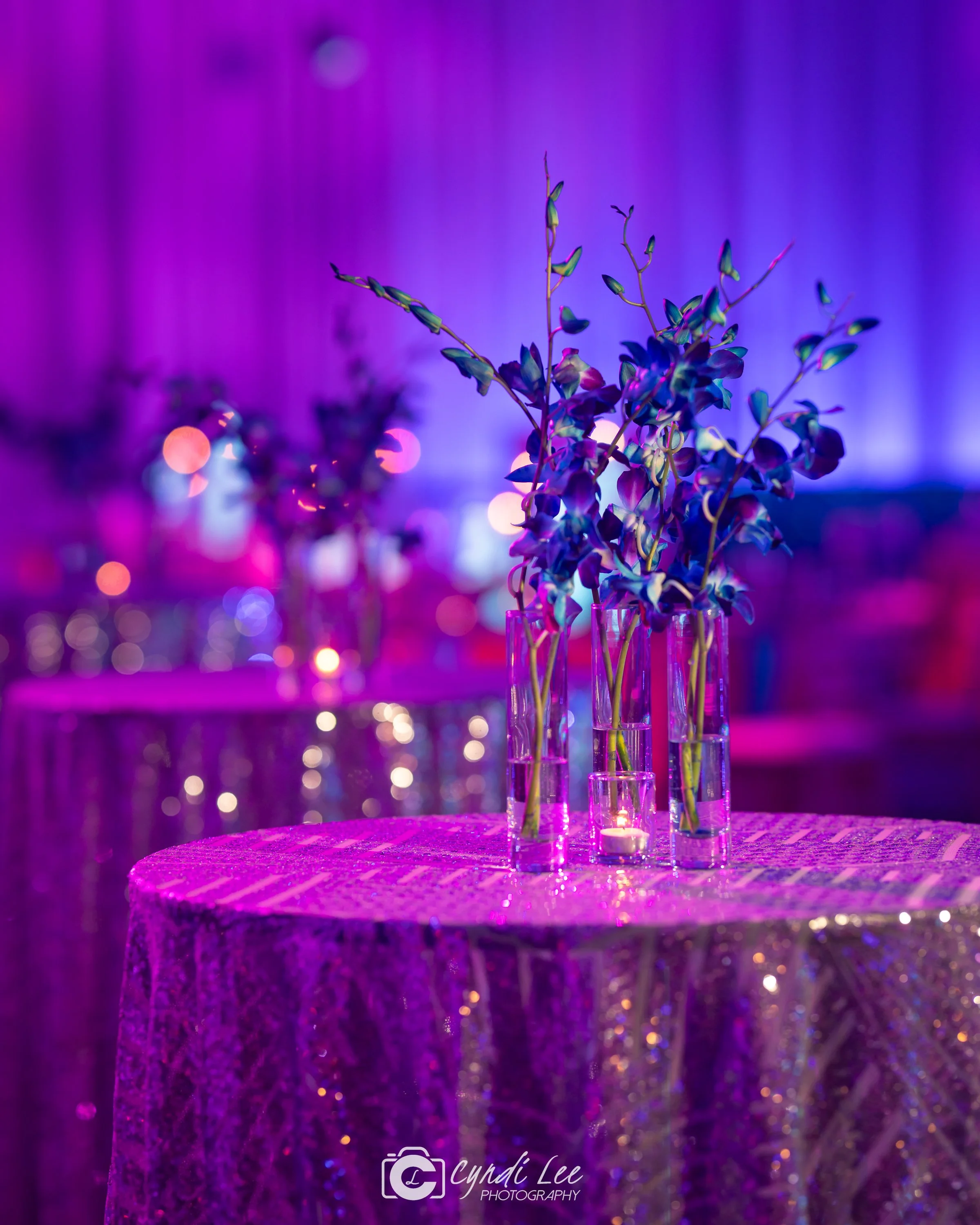 blue and purple orchids on a silver sequin tablecloth with pink lighting on it