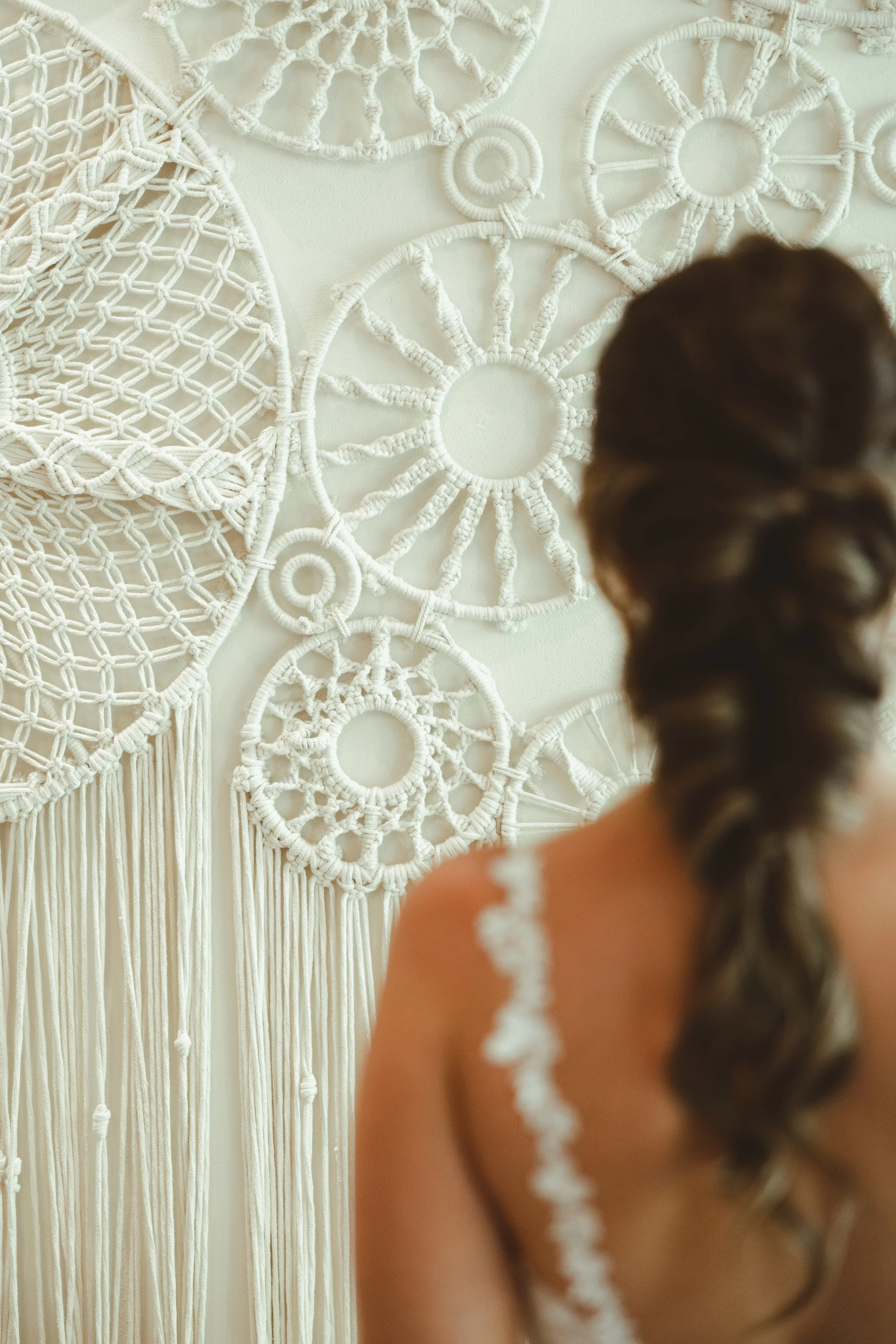Back of woman with braided hair in front of a wall of white macramé wall hangings with circular and spiral patterns.