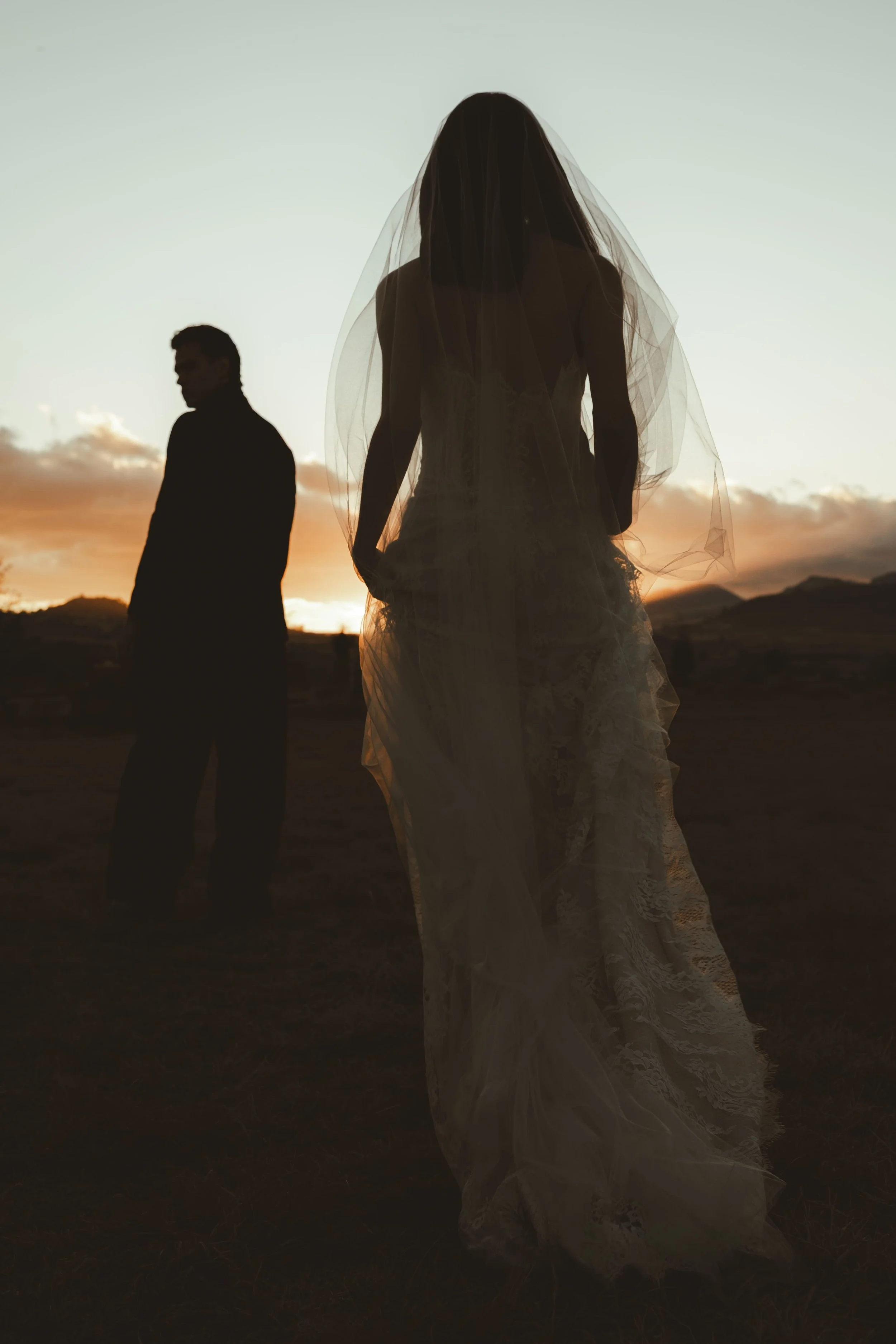 Silhouettes of a bride in a wedding dress with a veil and a groom in a suit standing in a landscape at sunset, mountains and clouds in the background of their wedding venue near mexico city.