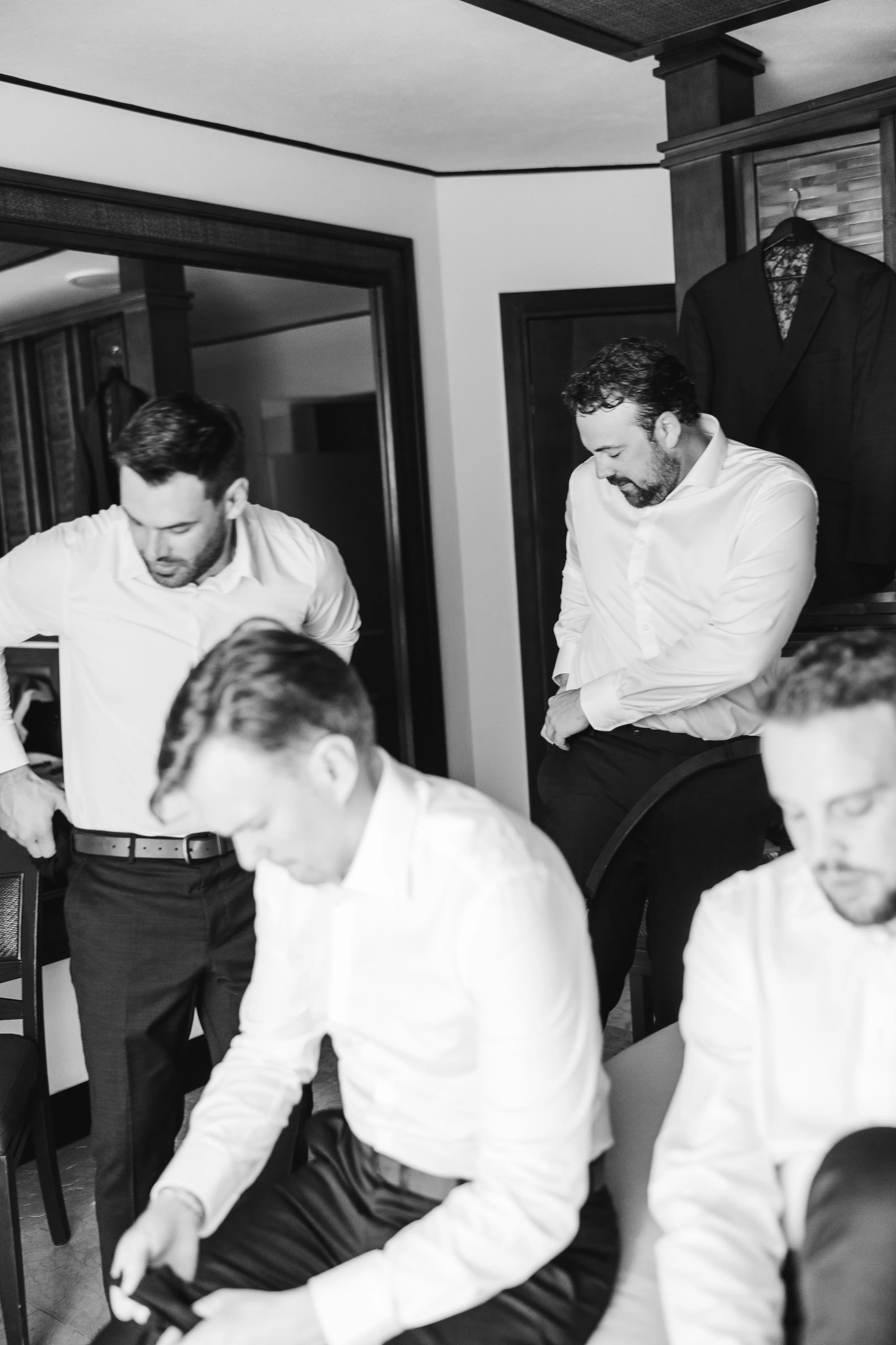 Groomsmen in white shirts getting ready in a room, some standing and some sitting, engaged in a candid, natural moment captured by the wedding photographer in cancun.