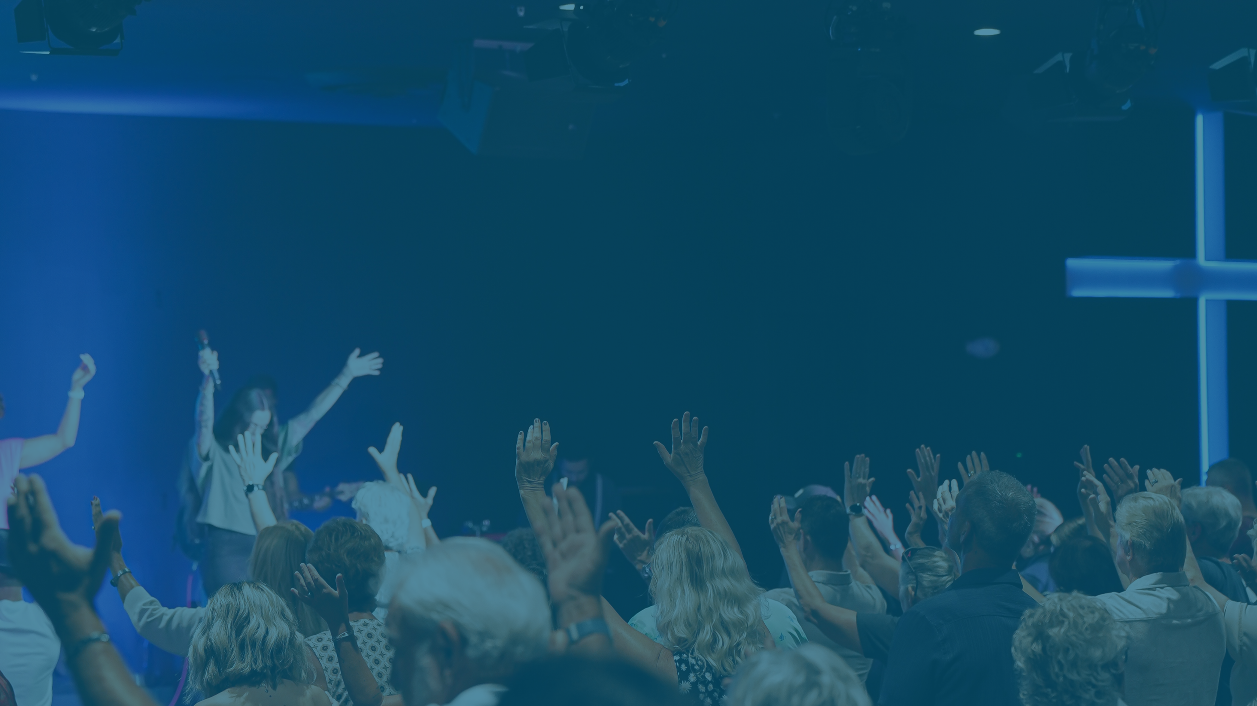 People raising their hands in an indoor auditorium or conference room during a concert or presentation.