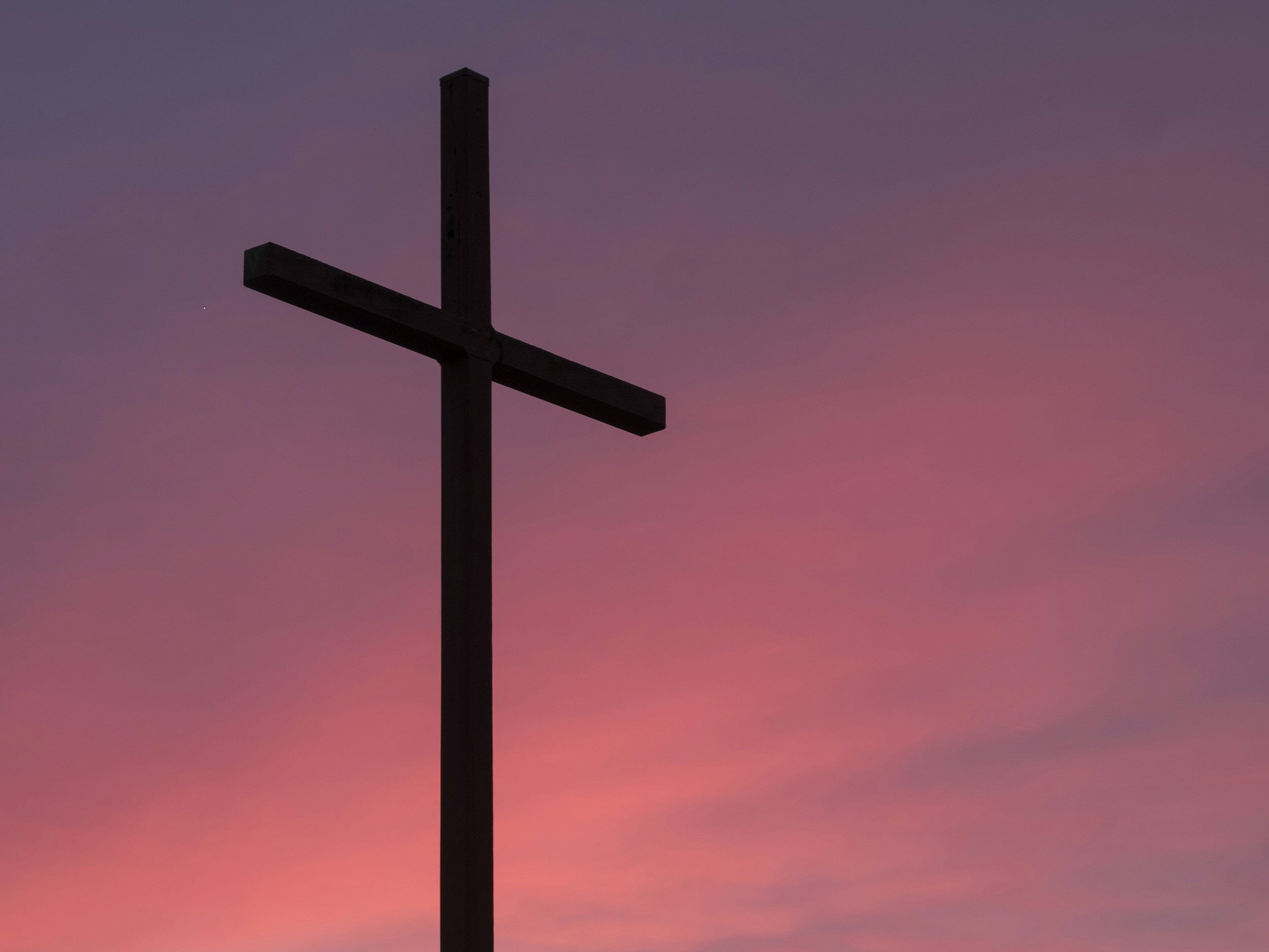 Silhouette of a cross against a pink and purple sunset sky.
