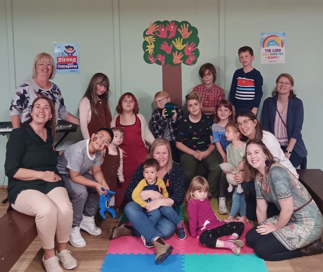 Group of children and adults in a Sunday School, with colorful wall decorations.